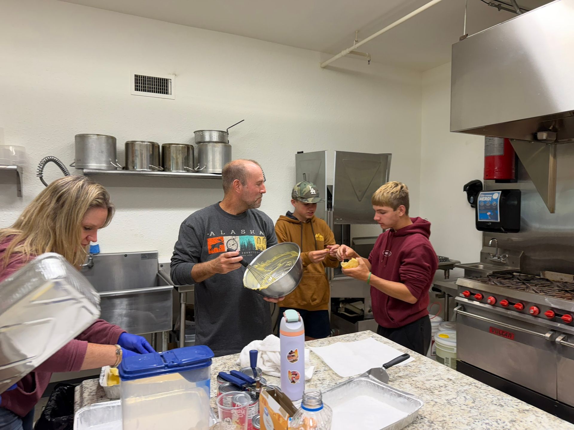 People preparing food together in a commercial kitchen, using trays and utensils.