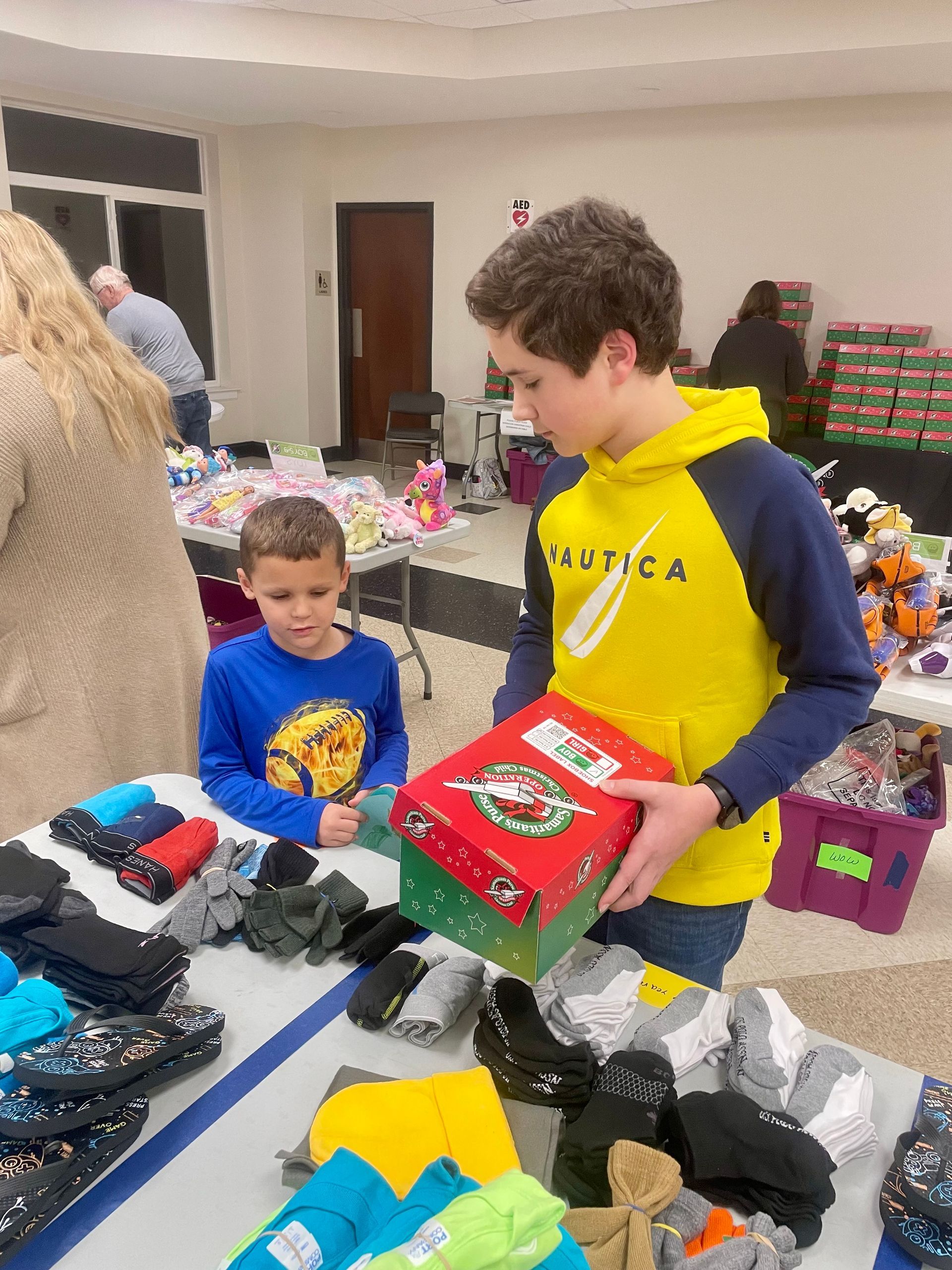 Children at a table sorting donated clothes and shoes into boxes at an indoor event