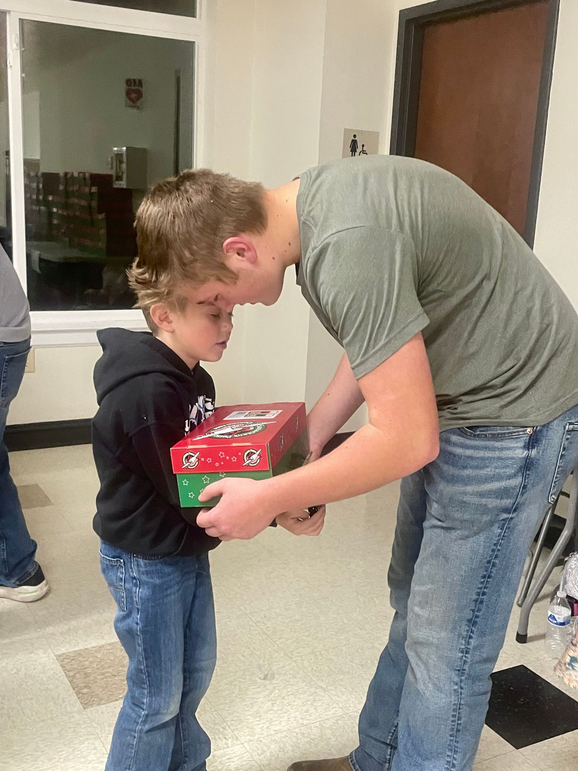Teenager helping a child hold a red box in a hallway