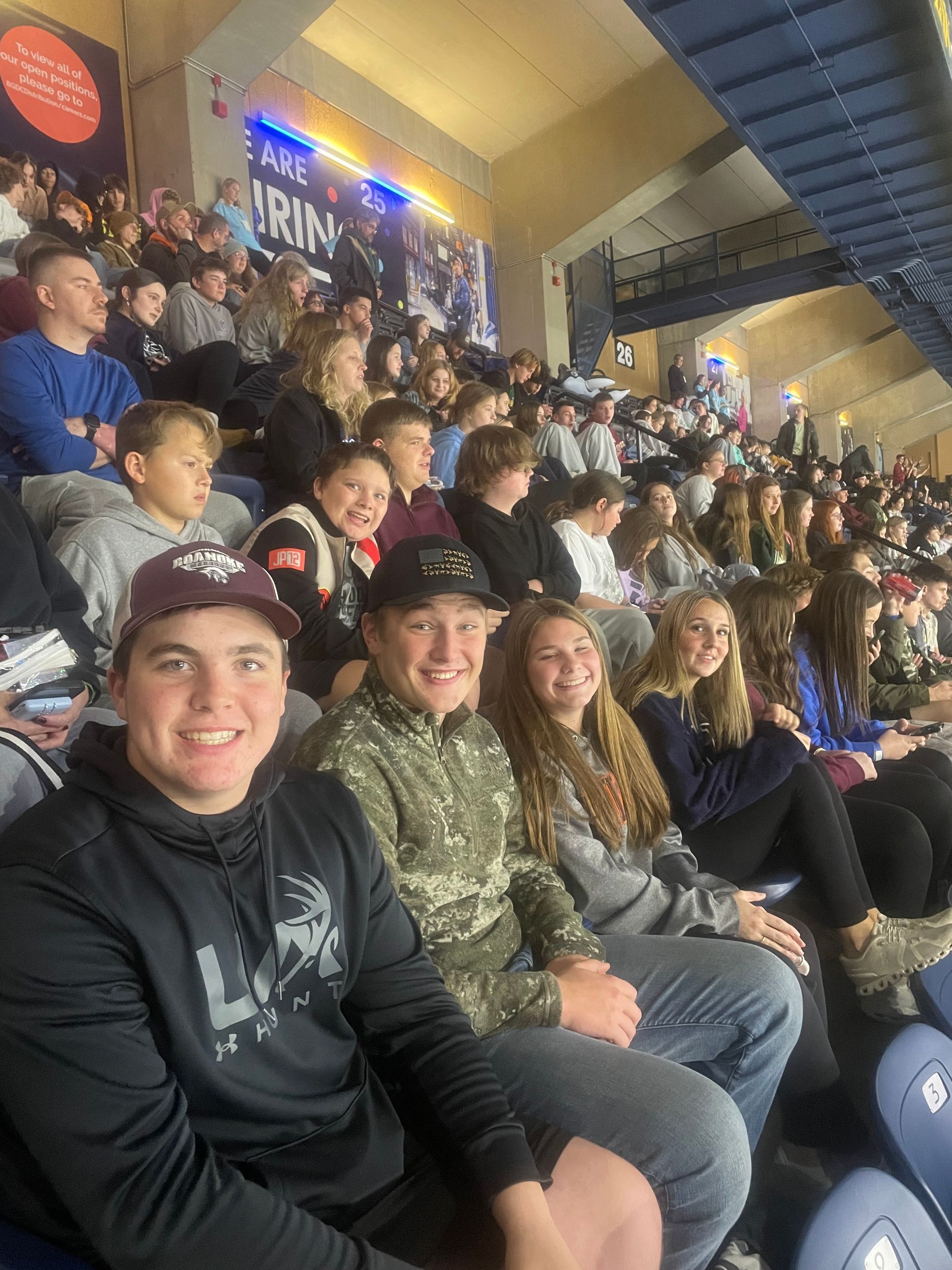 Crowded stadium stands with smiling spectators in dark jackets under bright arena lights