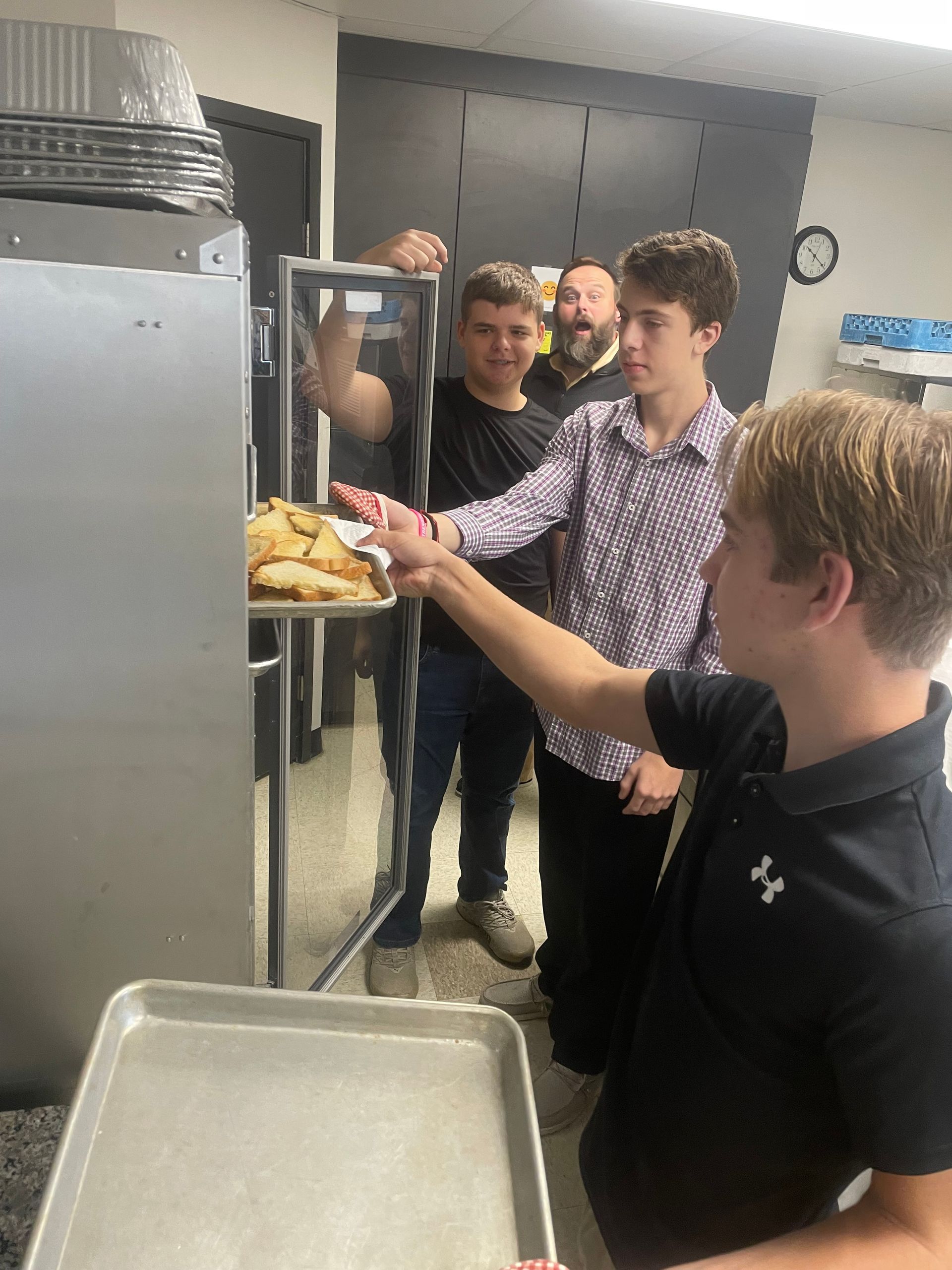 Teenagers in a kitchen reaching toward a tray of pastries by an oven