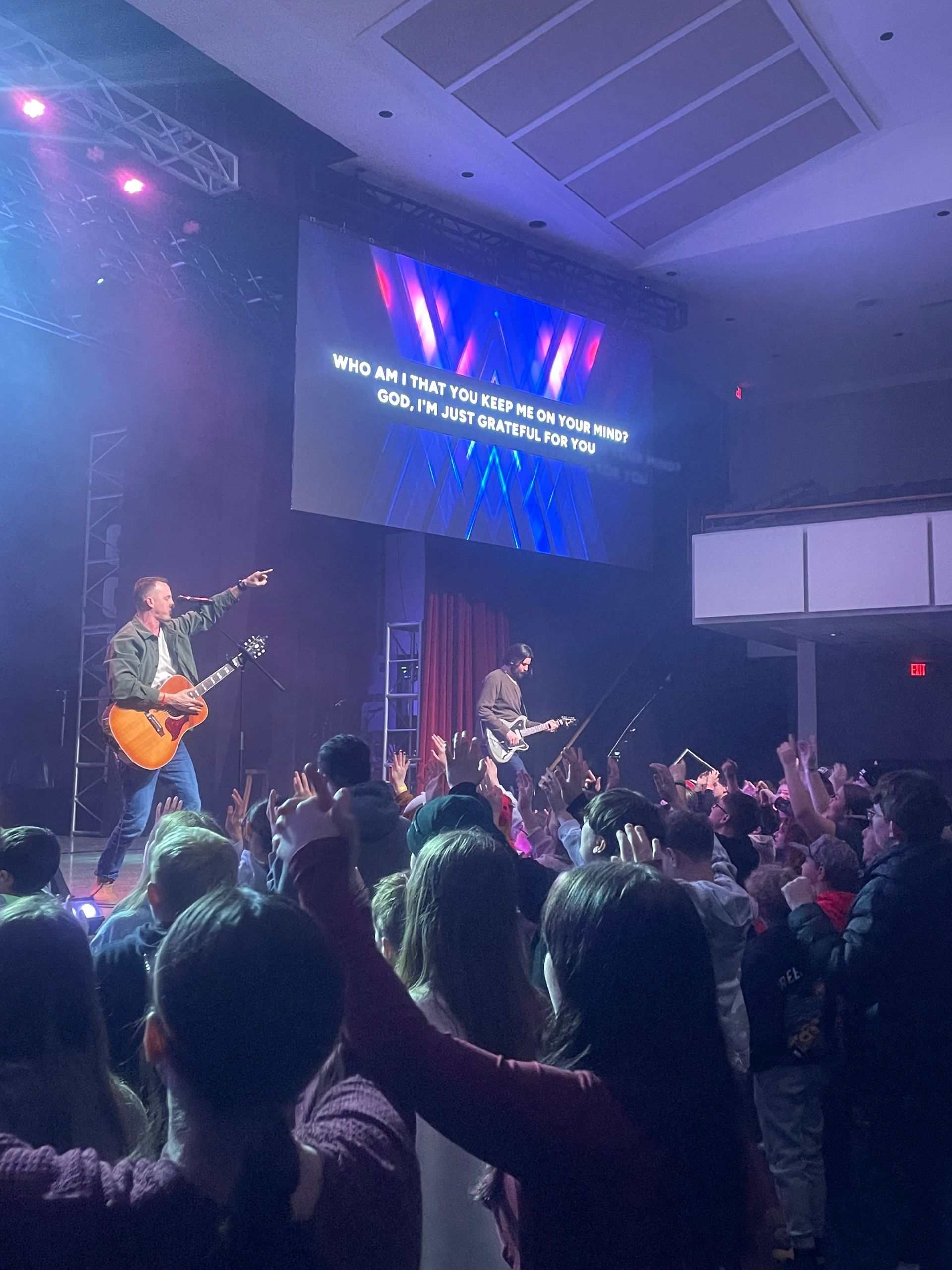 Concert crowd watching a live band on stage under colorful lights and a large screen