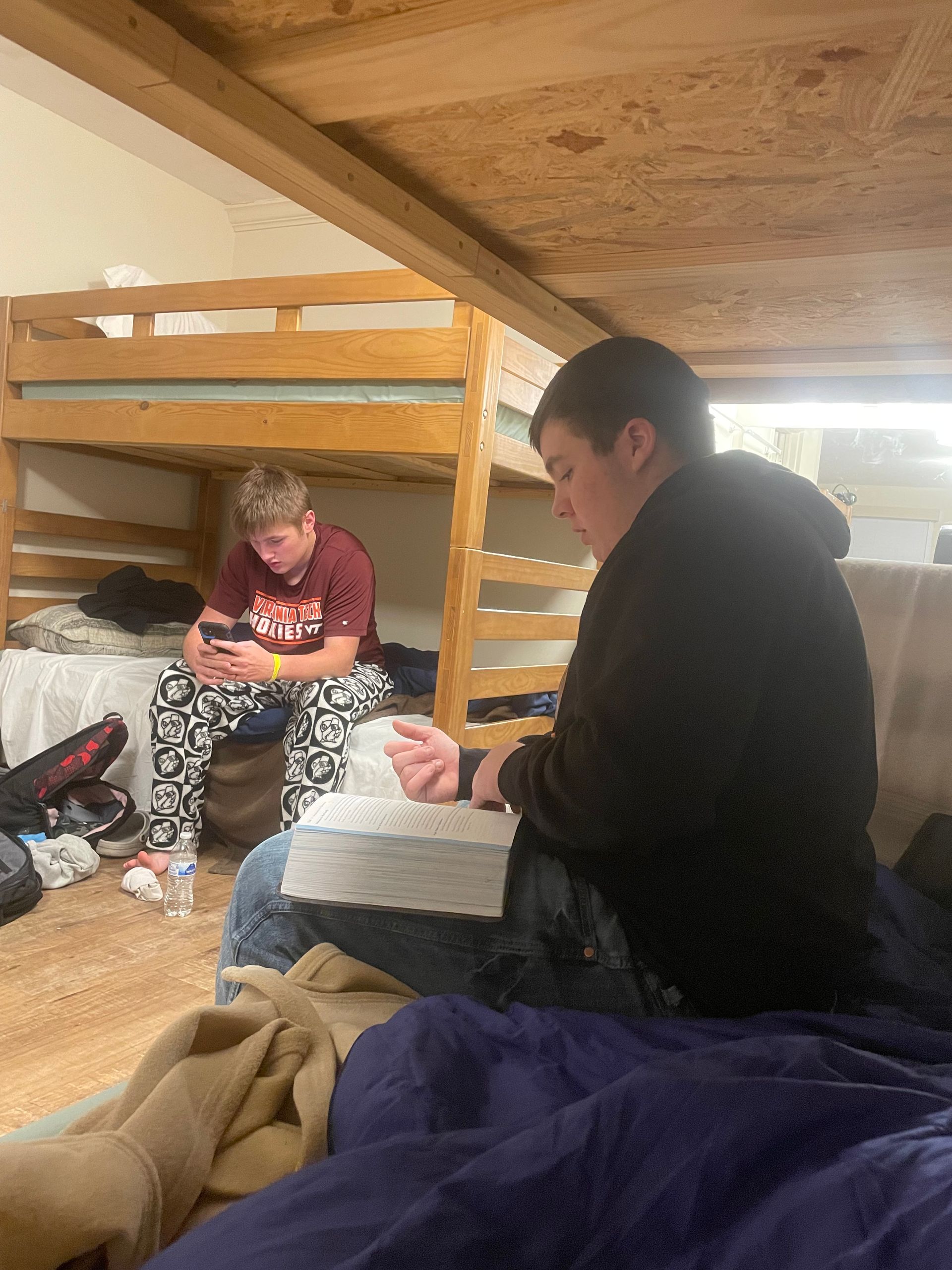 Two teenagers in a bunk room, one sitting on a lower bunk and one on a bed in the foreground.