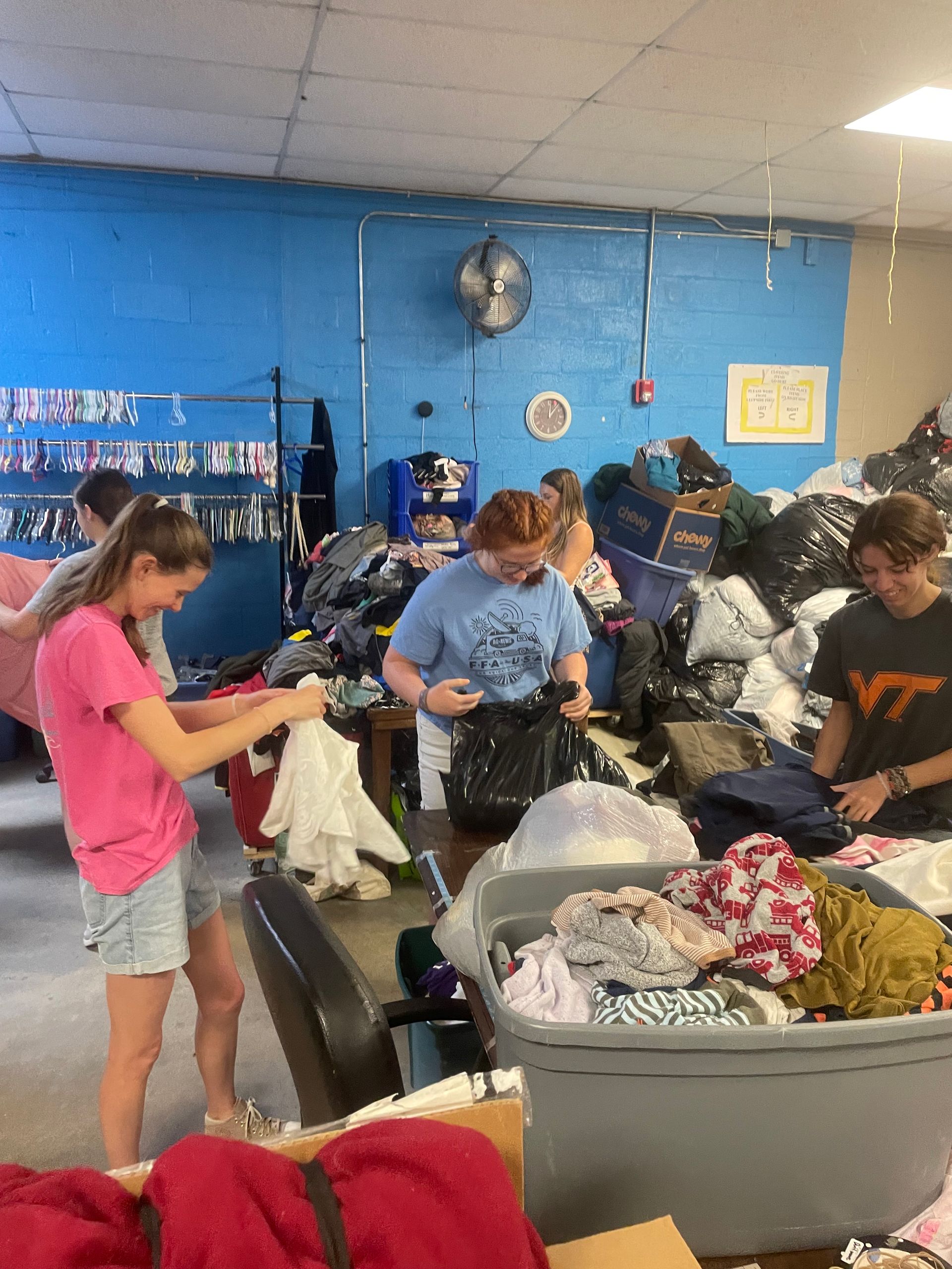 Teenagers sorting through bags and clothes in a crowded blue-walled laundromat.