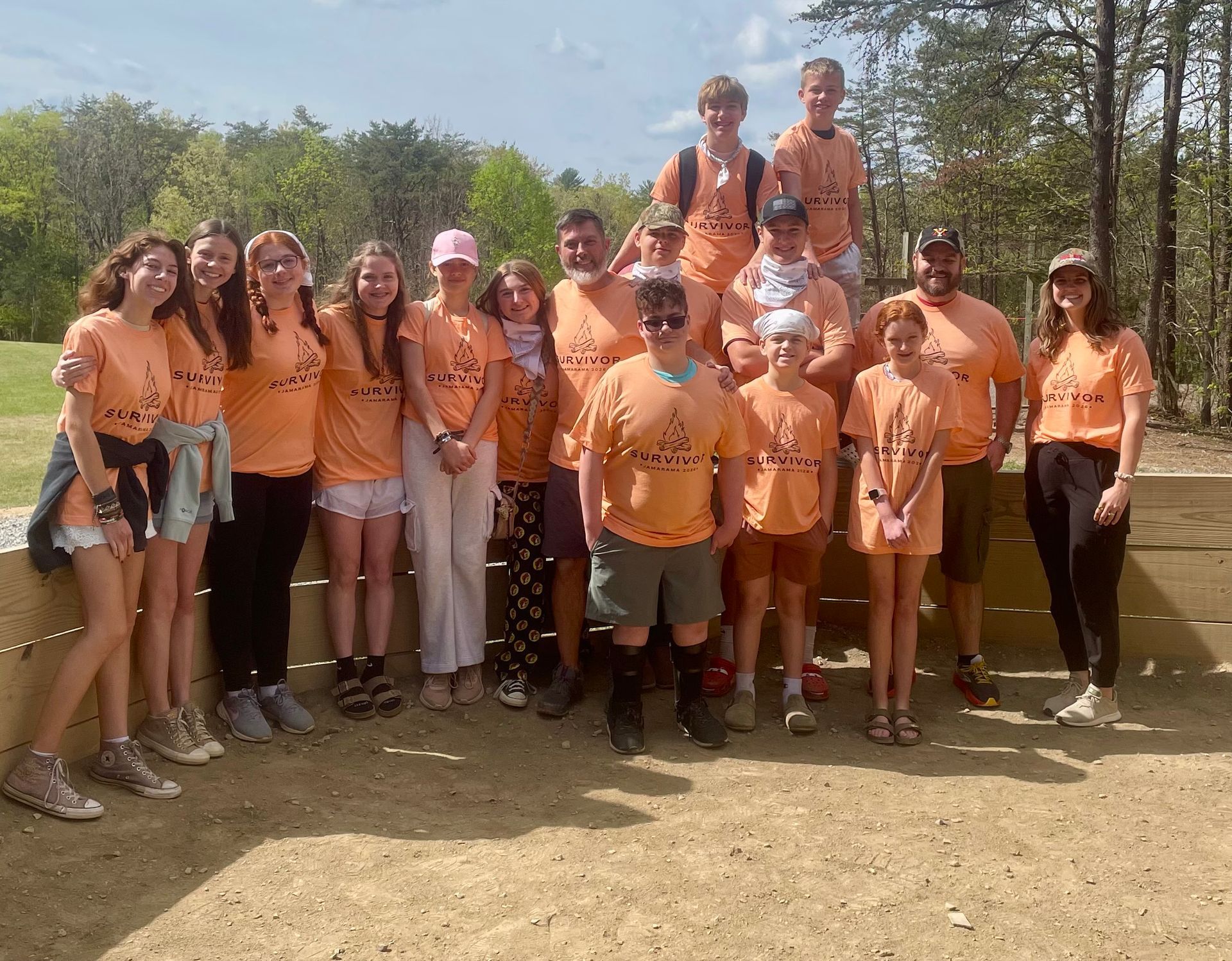 Group of teenagers in orange shirts posing outdoors in a sunny wooded area