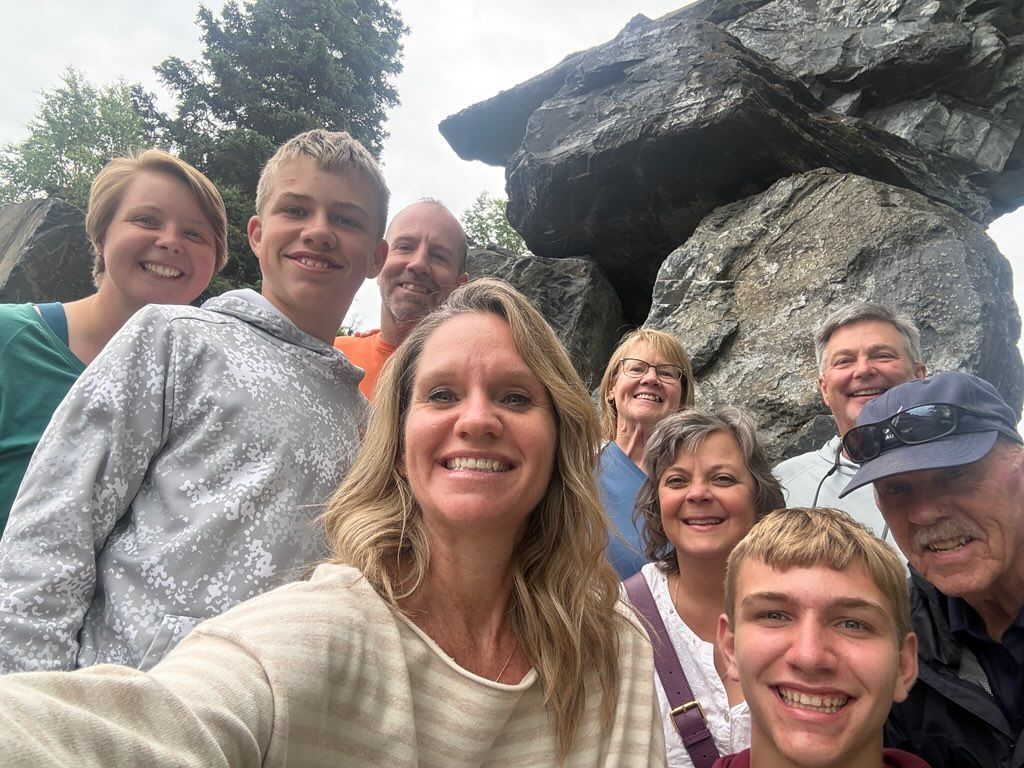 Group selfie of nine people smiling in front of large rocks outdoors