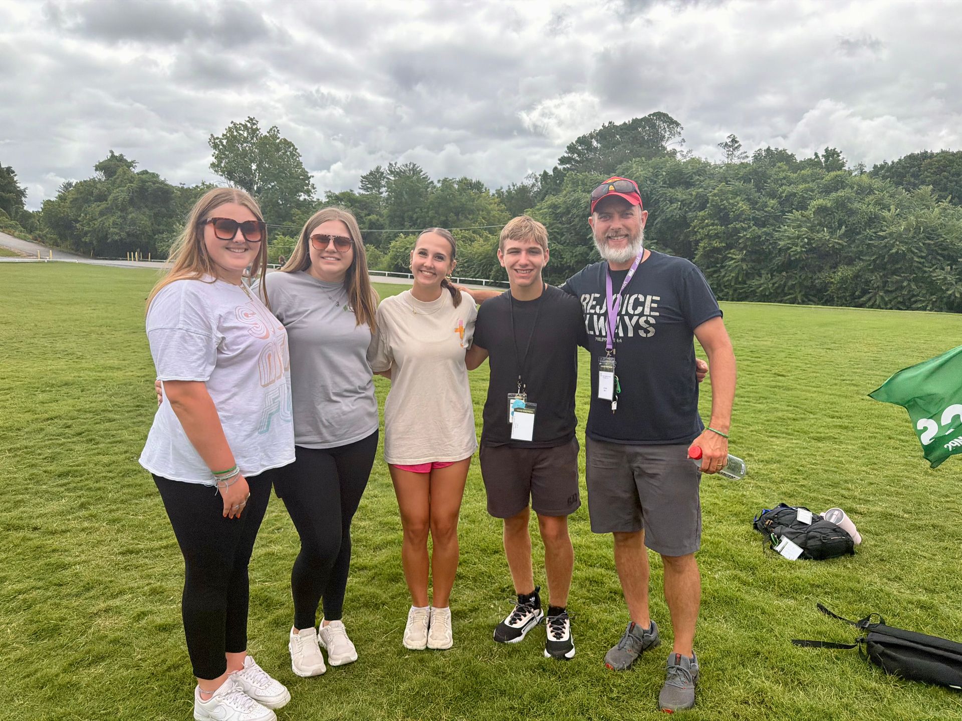 Four people posing together on a grassy field under cloudy skies