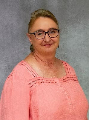 Smiling woman in glasses wearing a coral top against a gray backdrop