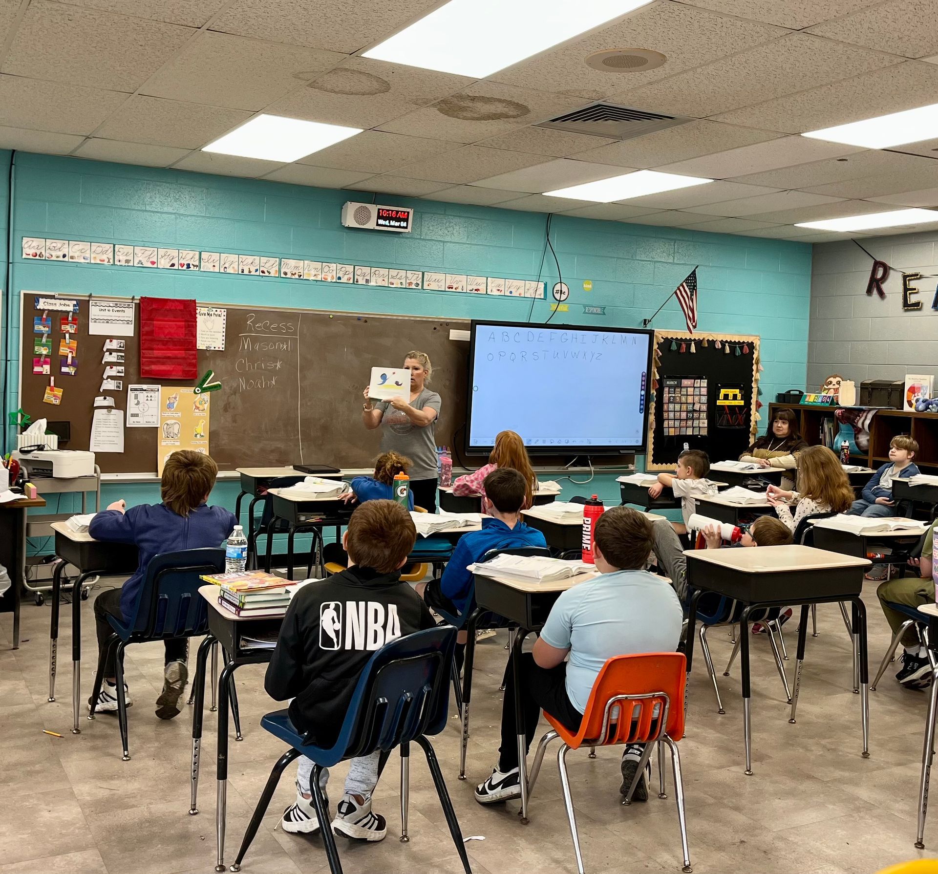 Classroom with students seated at desks facing a teacher and a large display screen