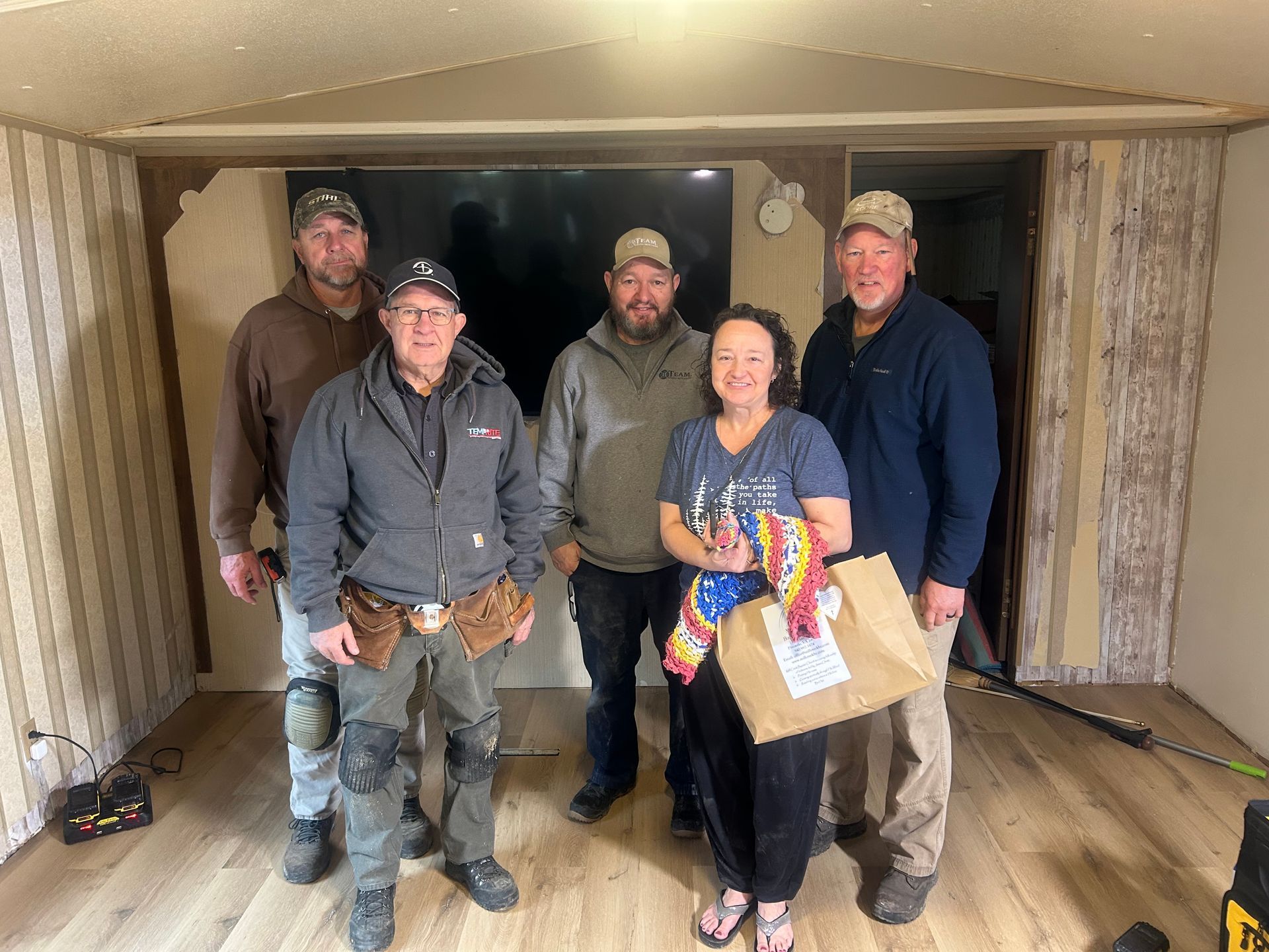 Five people standing together in a room, holding a box and smiling at the camera.