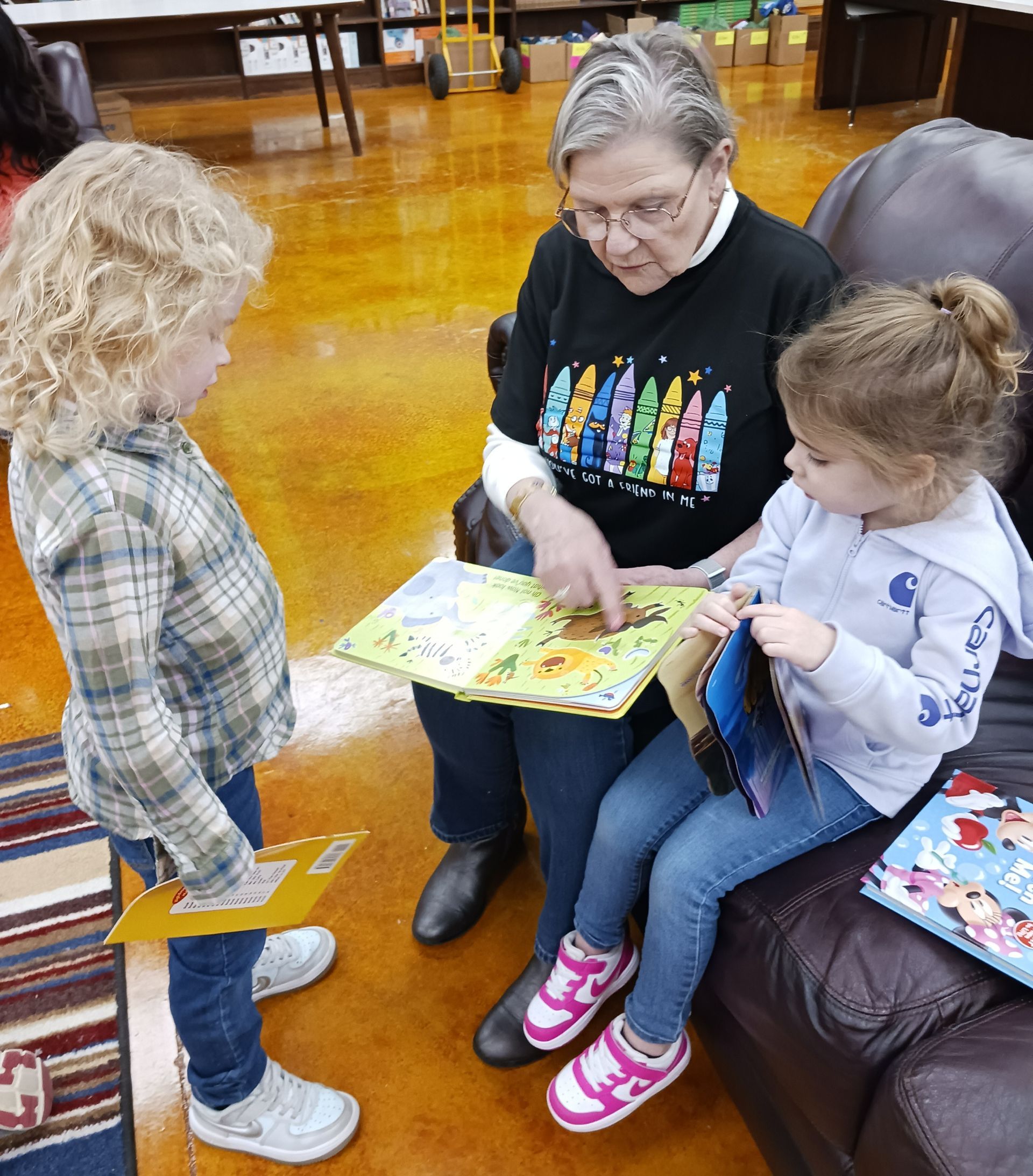 Adult reading a colorful book to two children in a cozy seating area