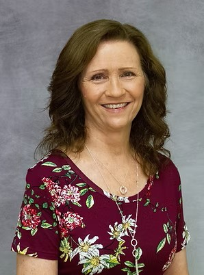 Smiling woman in a burgundy floral top against a gray background