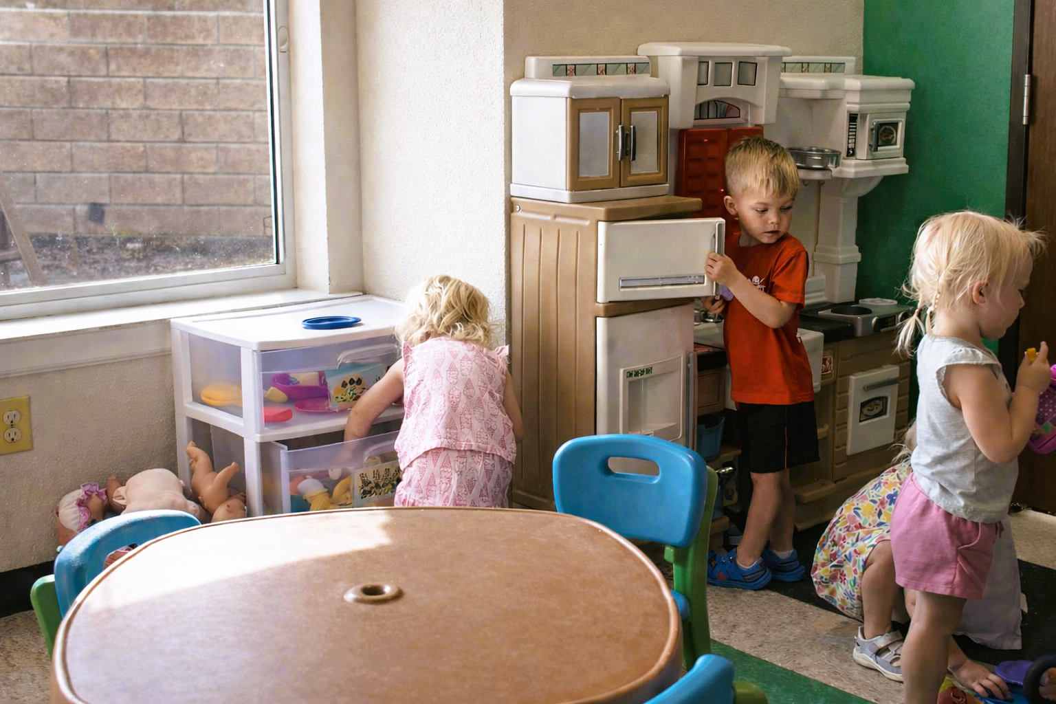 Children playing in a classroom with toy kitchens and a round table