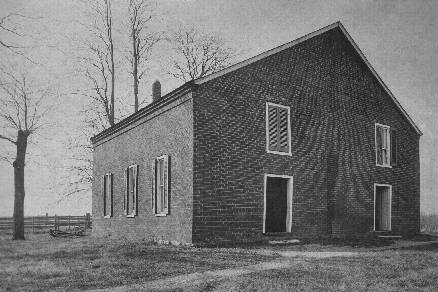Old brick church with dark roof in a sparse rural yard, viewed in black and white.