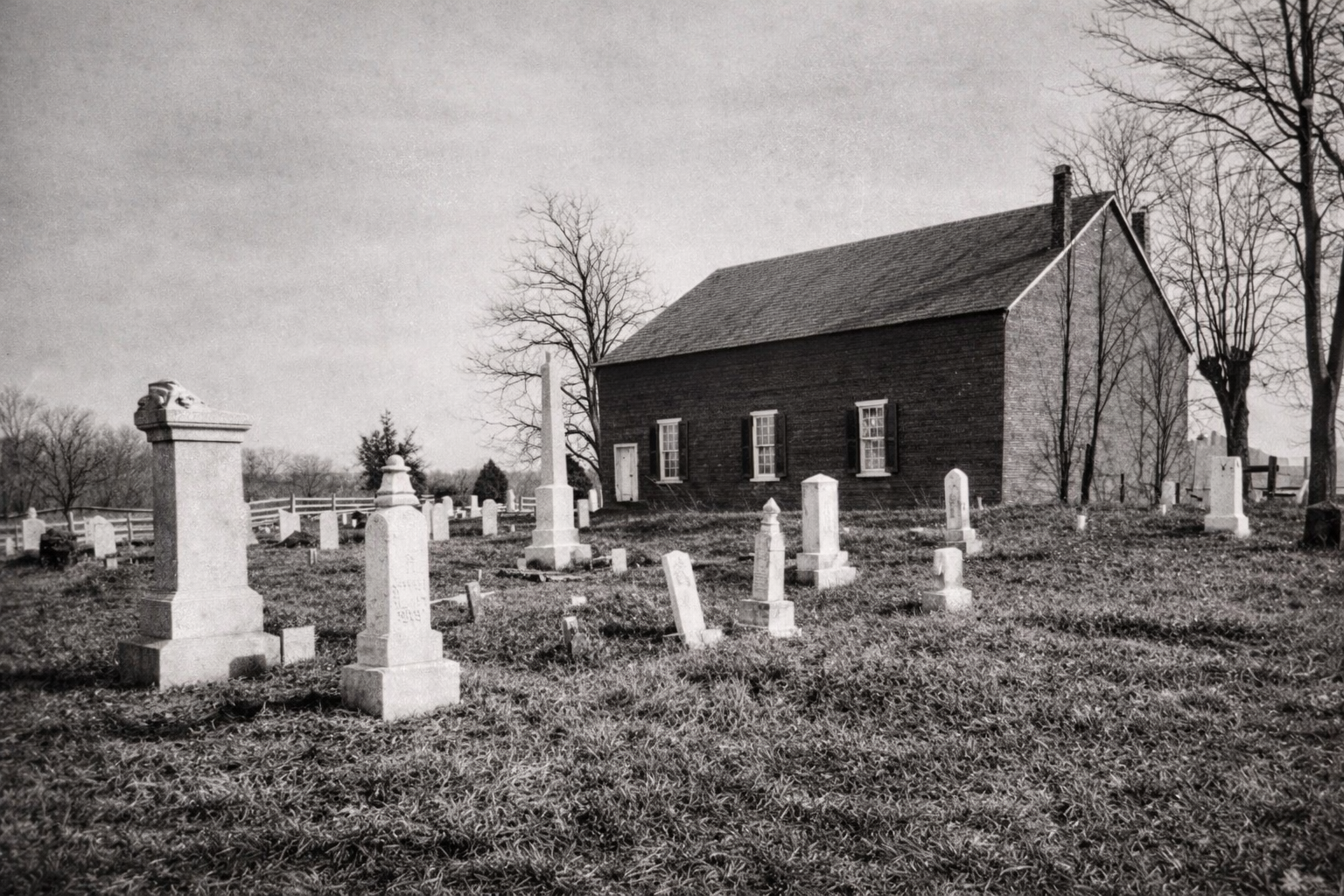 Old black-and-white photo of a small church with a graveyard and headstones in front