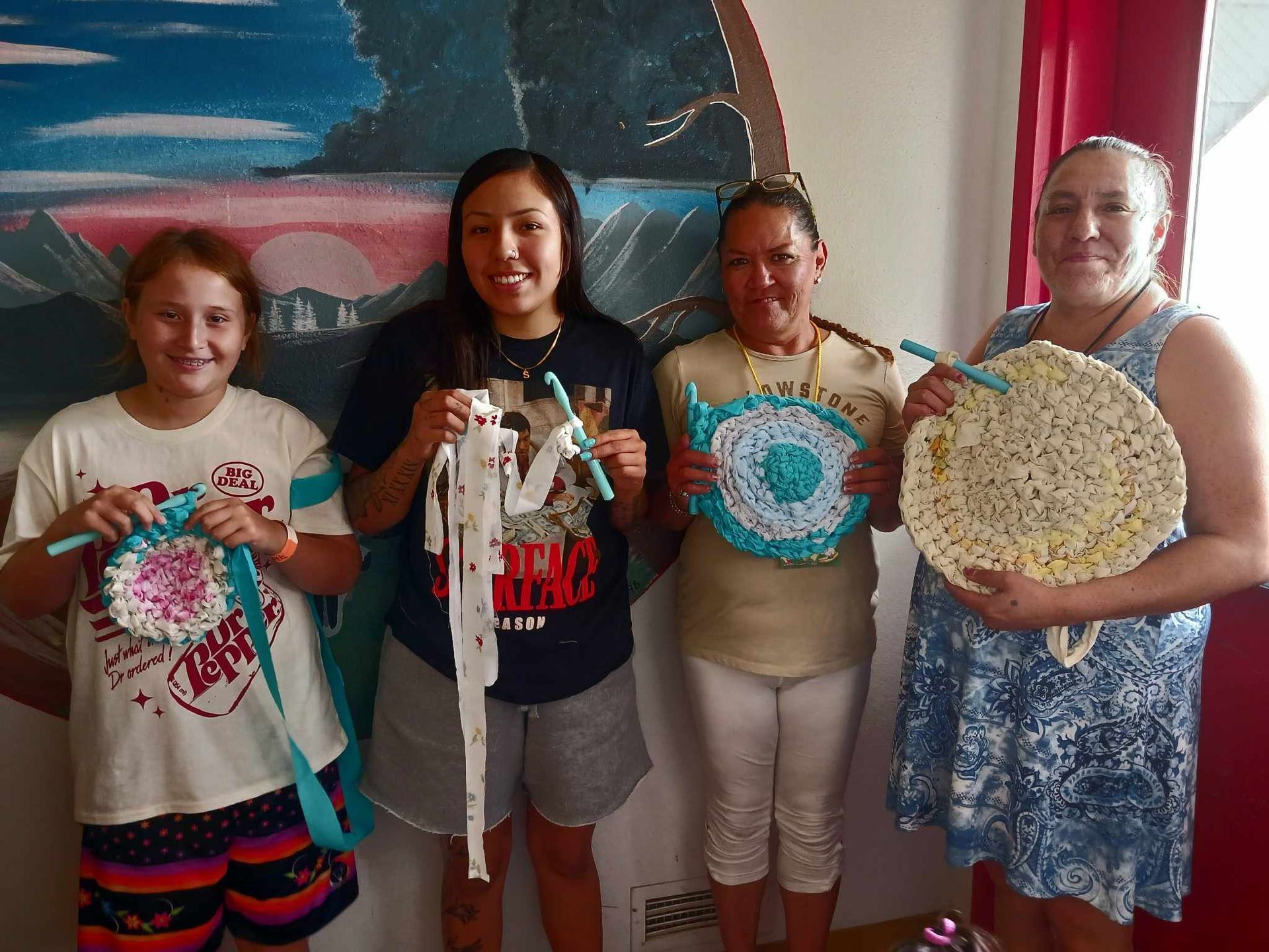 Four people standing indoors holding decorated circular craft pieces, smiling at the camera.