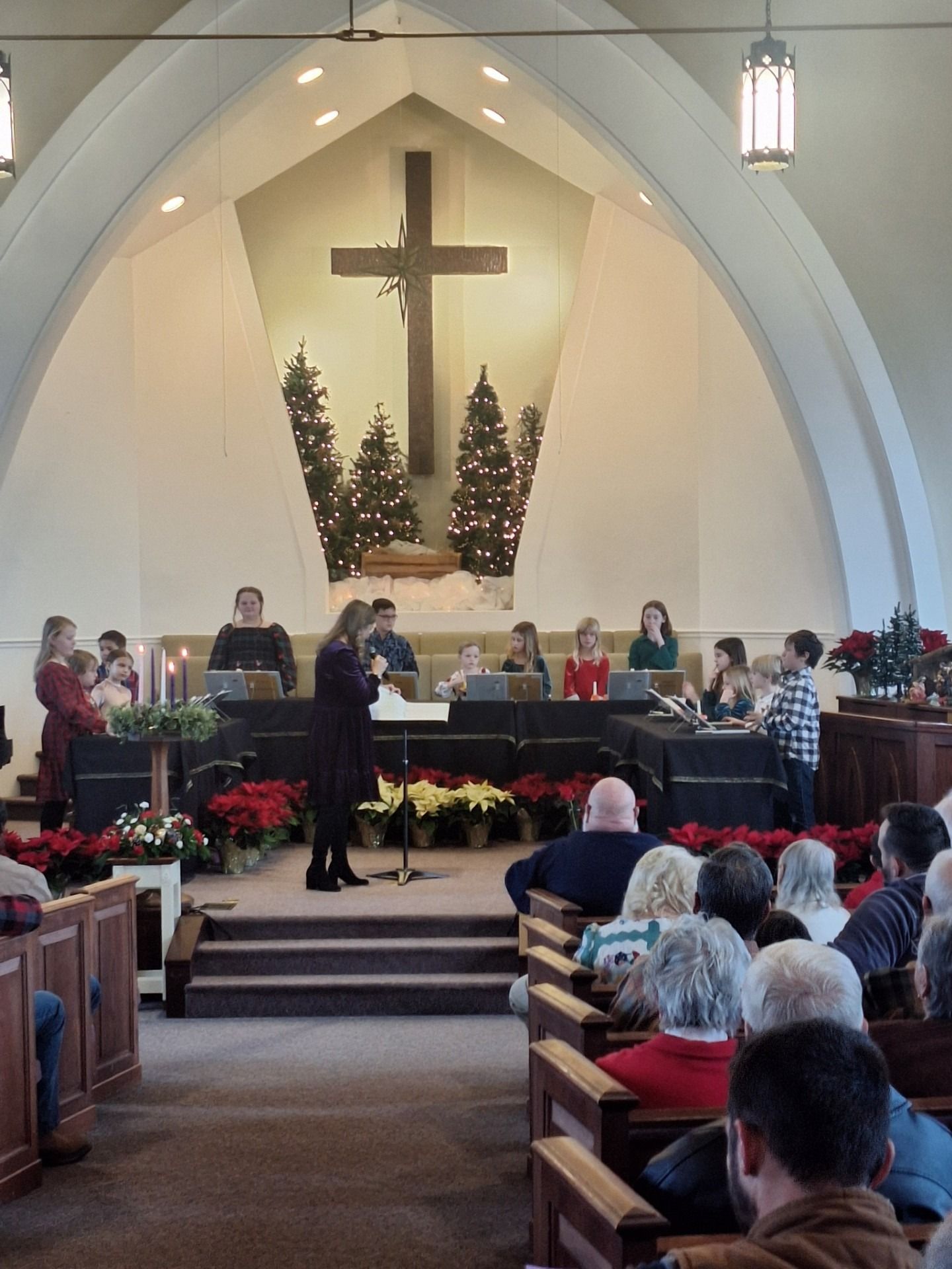 Childrens choir performing in front of a large cross, with Christmas decorations and seated congregation.