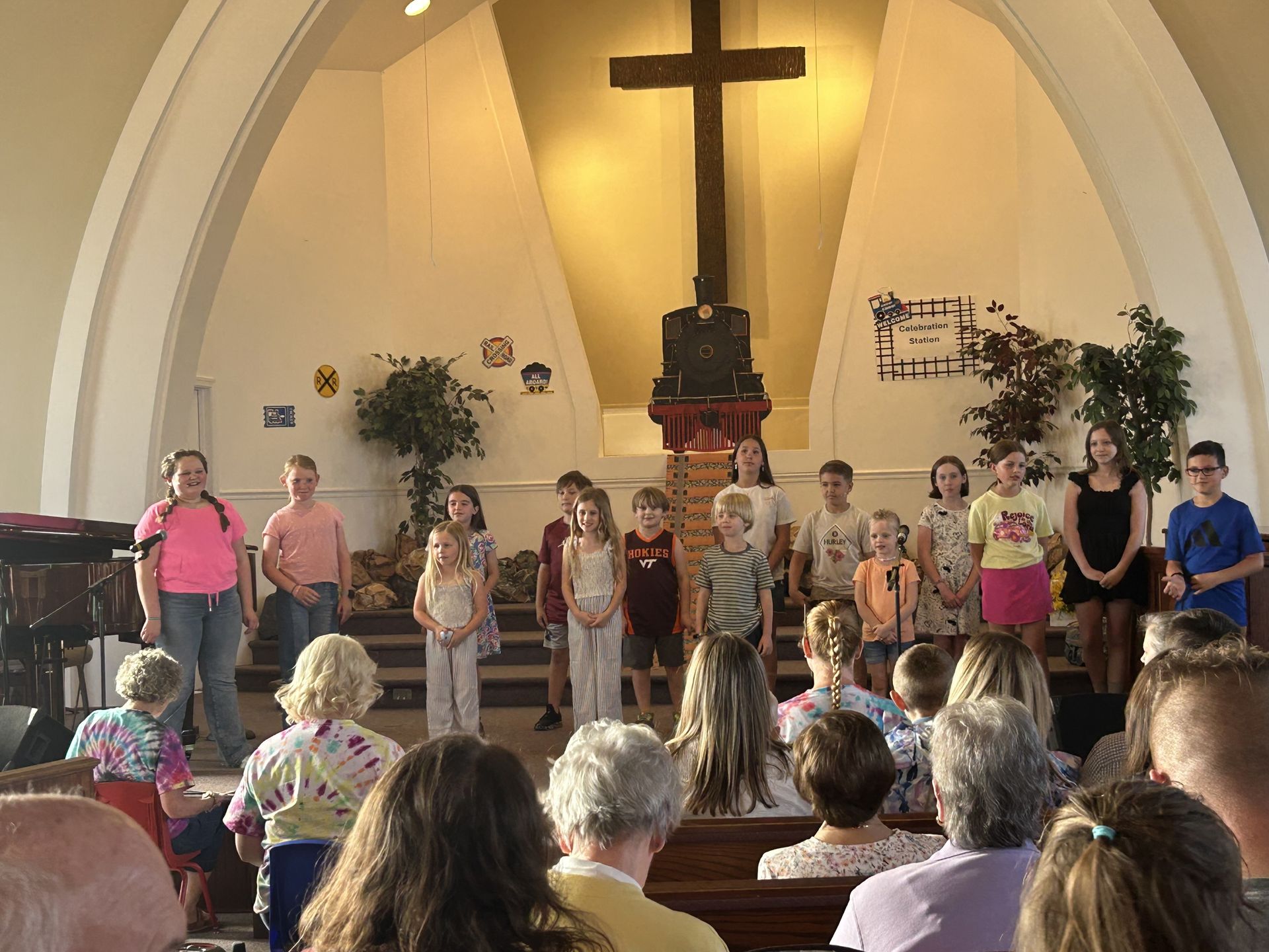 Kids standing at the front of a church sanctuary with a large cross behind them