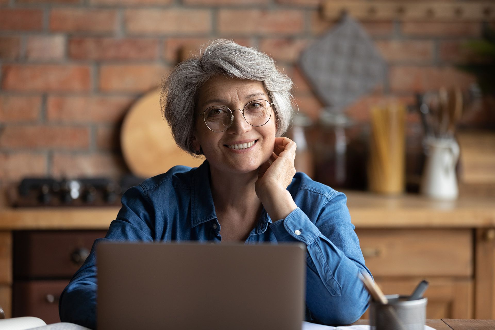 Smiling person in glasses sitting at a laptop in a cozy kitchen