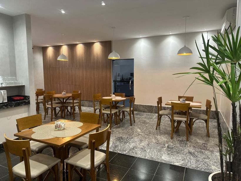 Interior de restaurante com mesas, cadeiras e iluminação suspensa. Paredes de madeira em tons claros