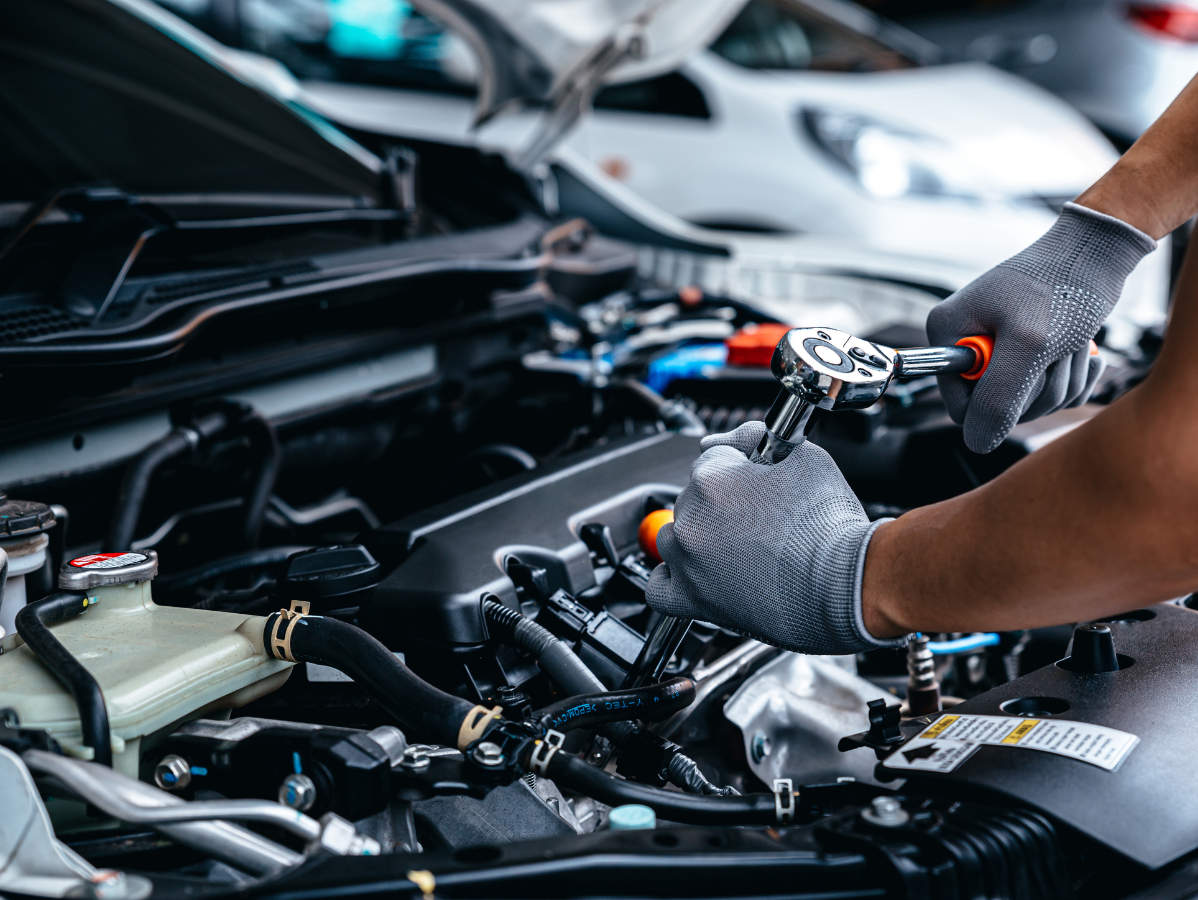 Mechanic working on a car engine with a wrench. Wearing gray gloves, in a garage setting.