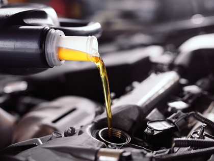 Oil being poured from a black container into a car engine, filling the reservoir.
