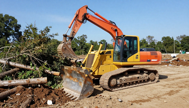 Orange excavator clearing tree debris on a dirt site