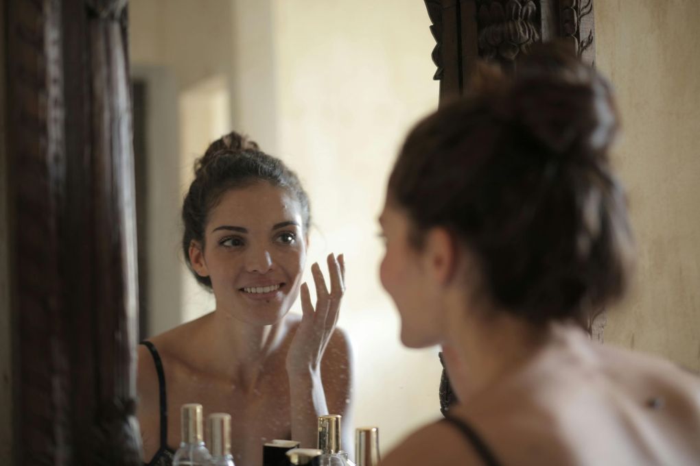 A woman with a towel wrapped around her shoulders is smiling and touching her neck.
