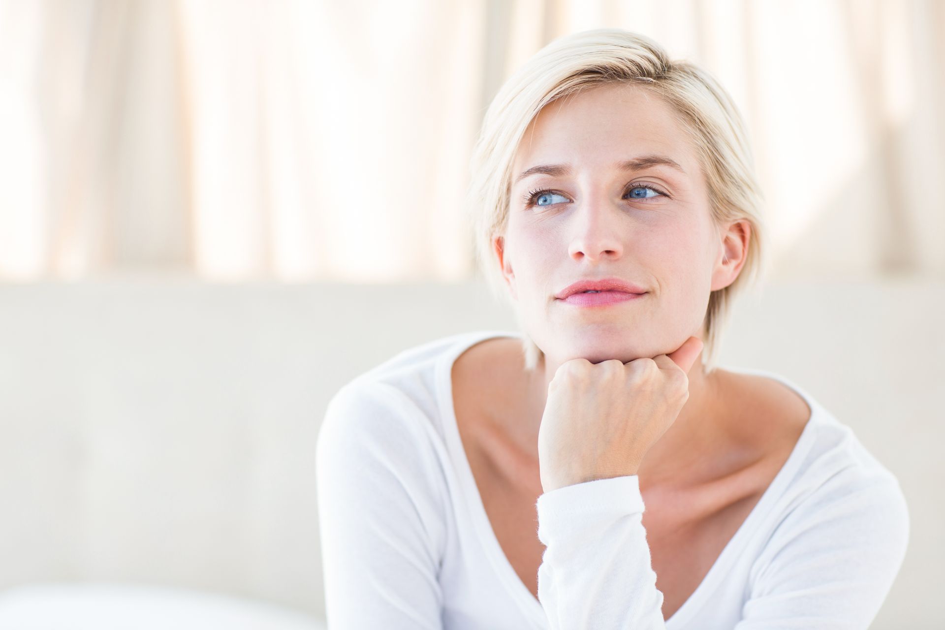 A woman is sitting on a couch with her hand on her chin and looking up.