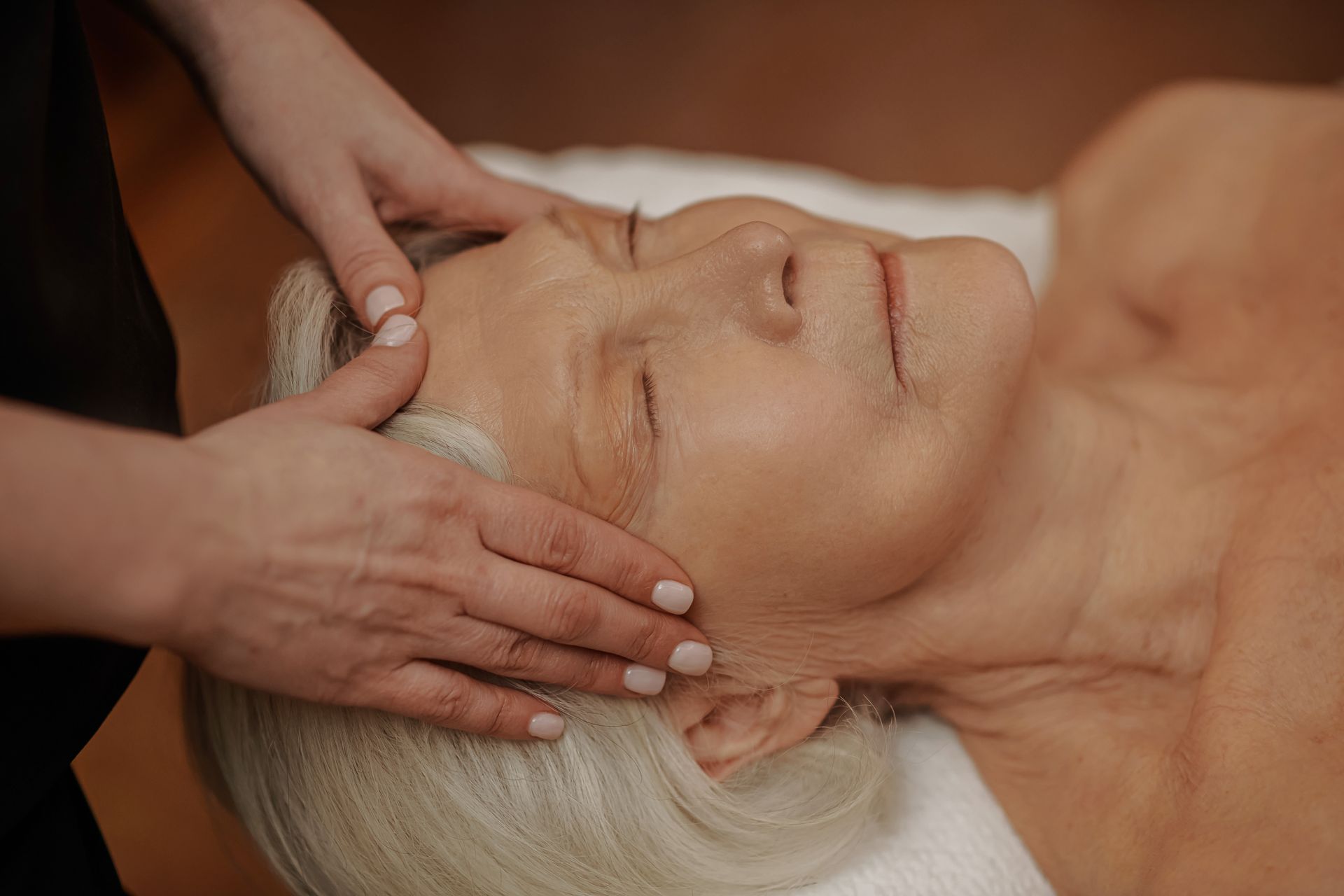 Hands gently giving a facial massage to a relaxed woman lying on a spa table