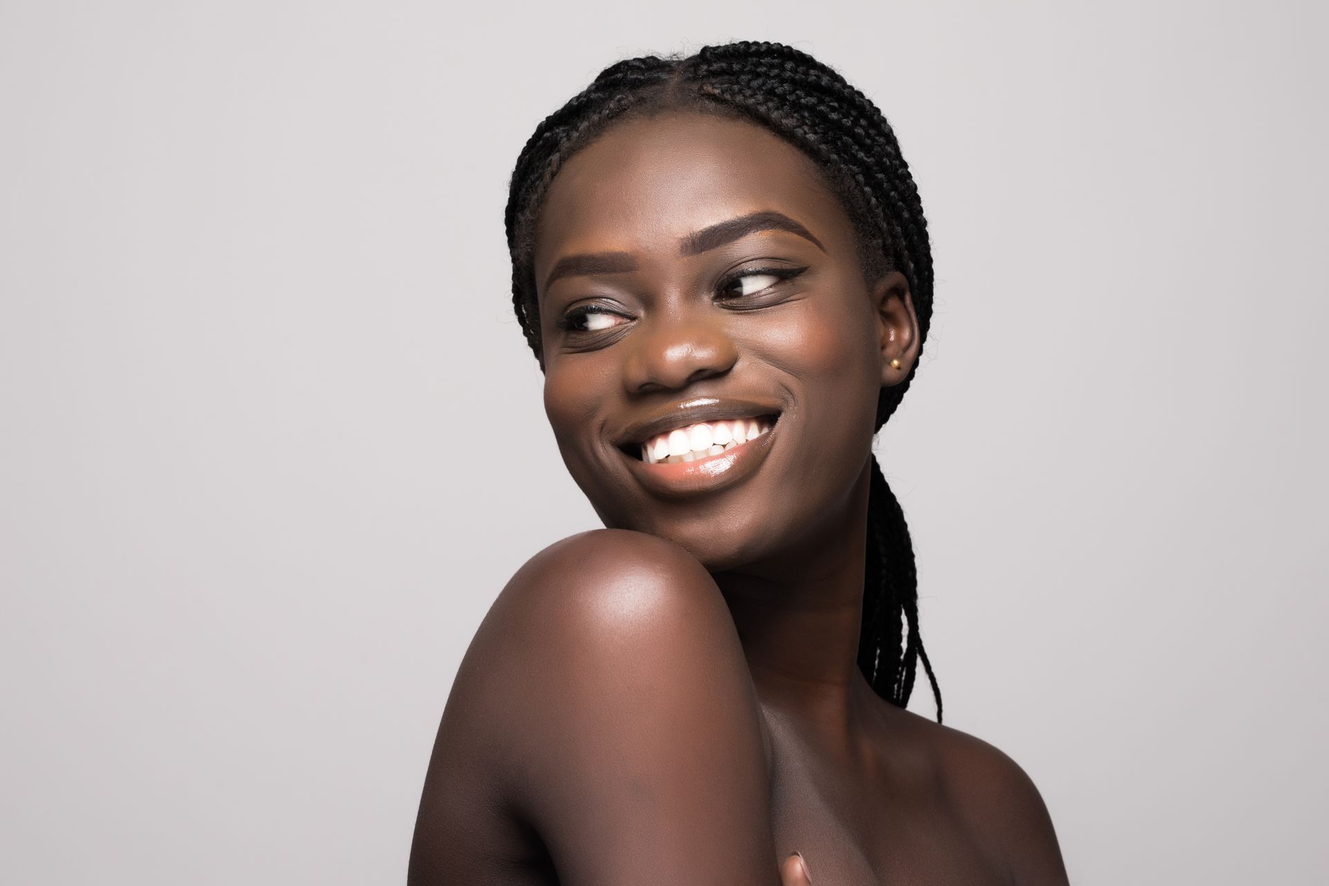 A woman with braids is smiling and looking over her shoulder.