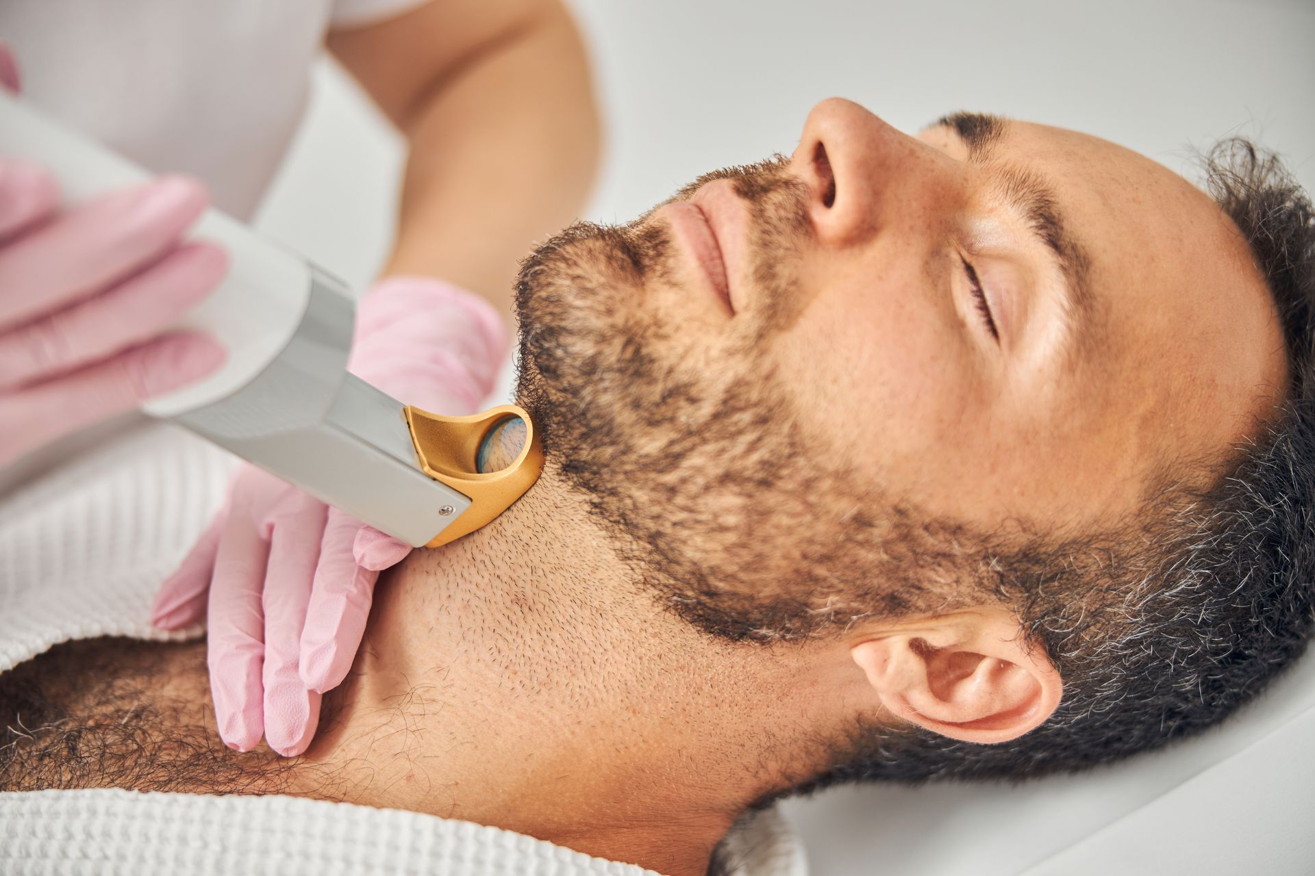 A man is getting a laser hair removal treatment on his beard.