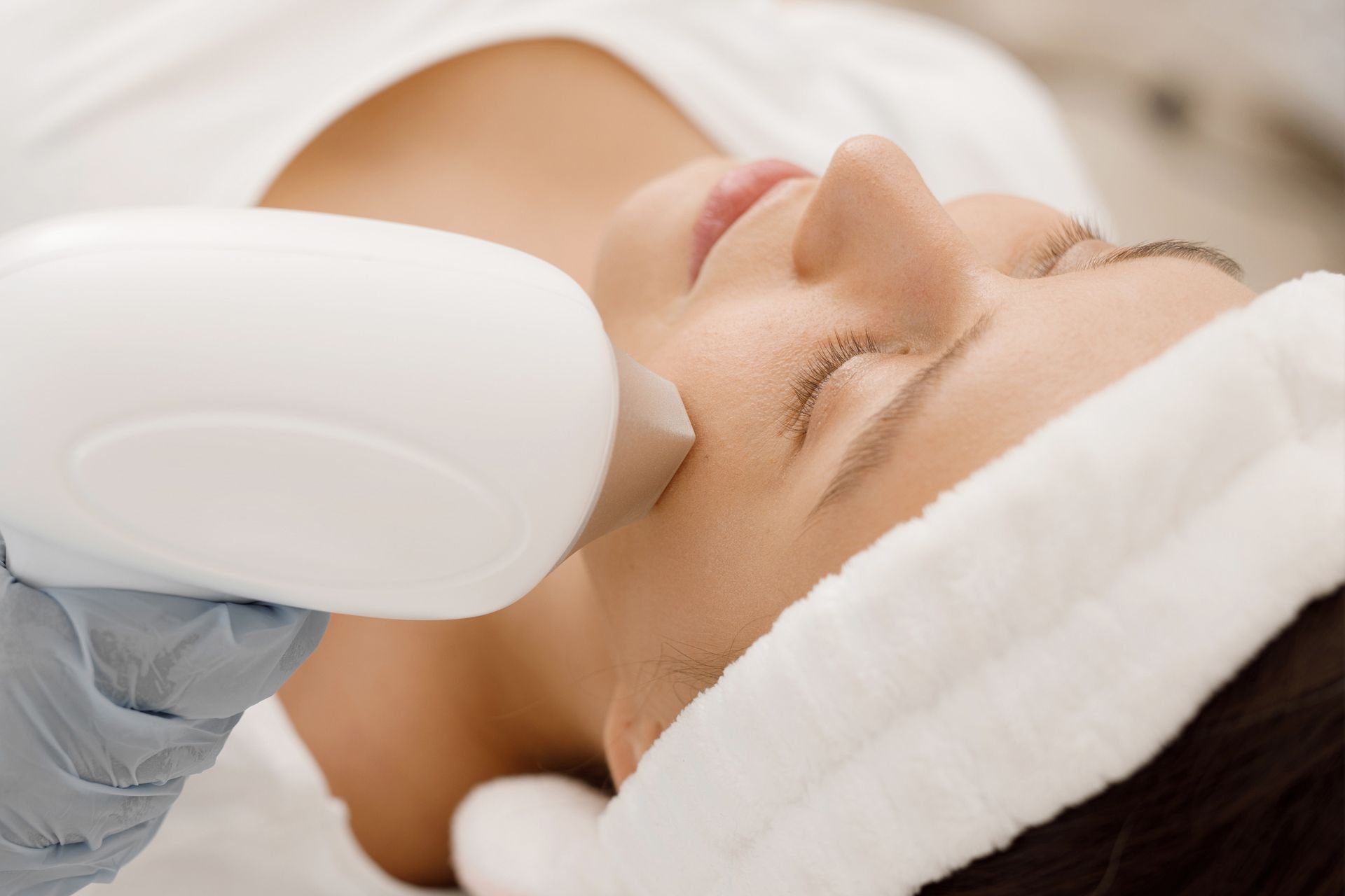 Person receiving a facial treatment with a handheld device and white headband in a spa setting