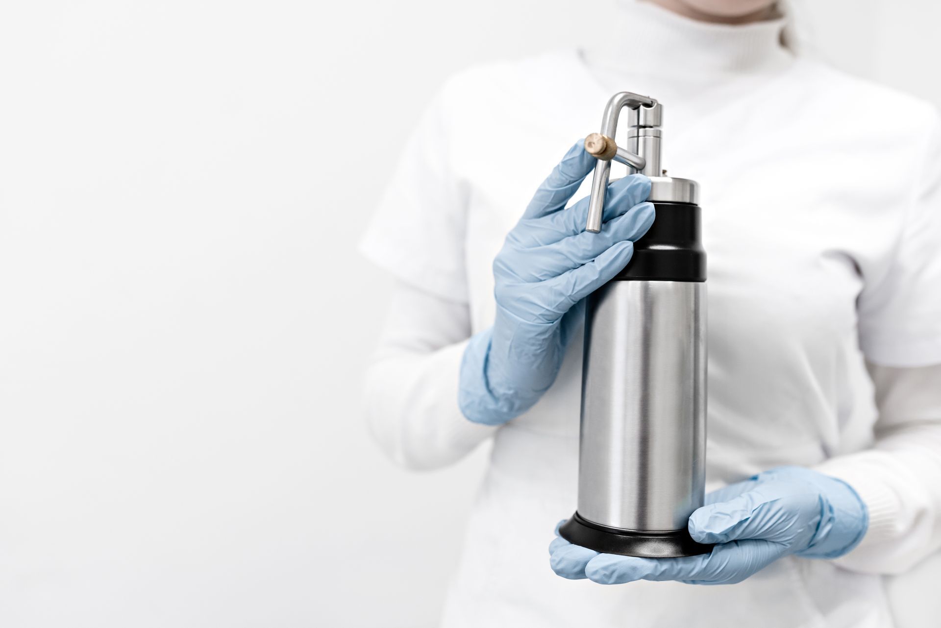 A woman in a white coat and blue gloves is holding a bottle of liquid nitrogen.