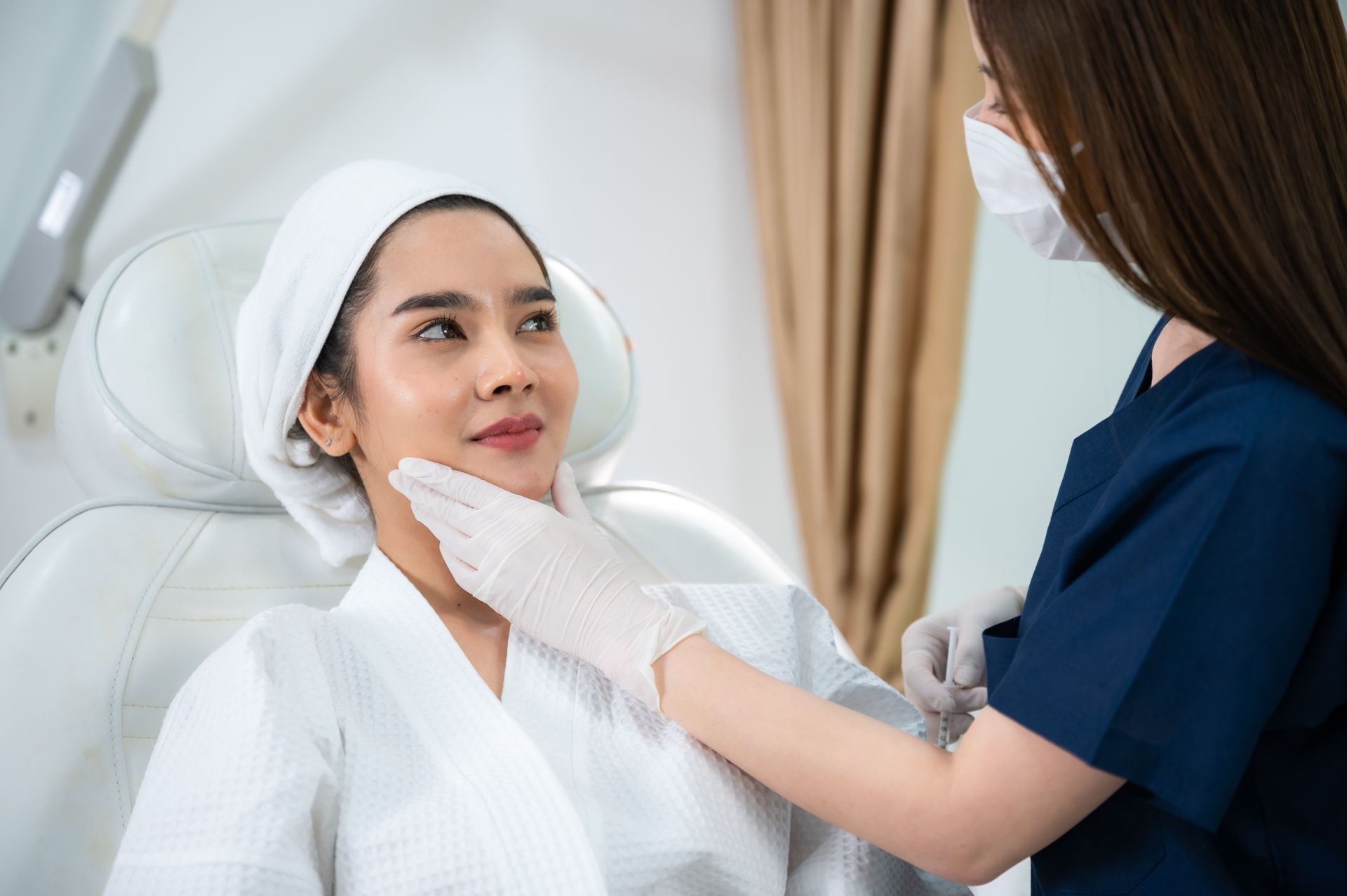 A clinician examines a patient’s face in a bright medical spa room.