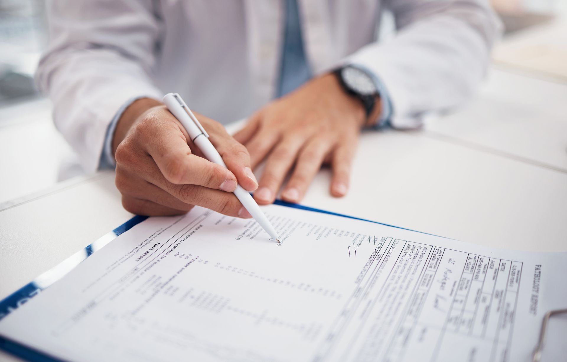 A doctor is writing on a clipboard with a pen.