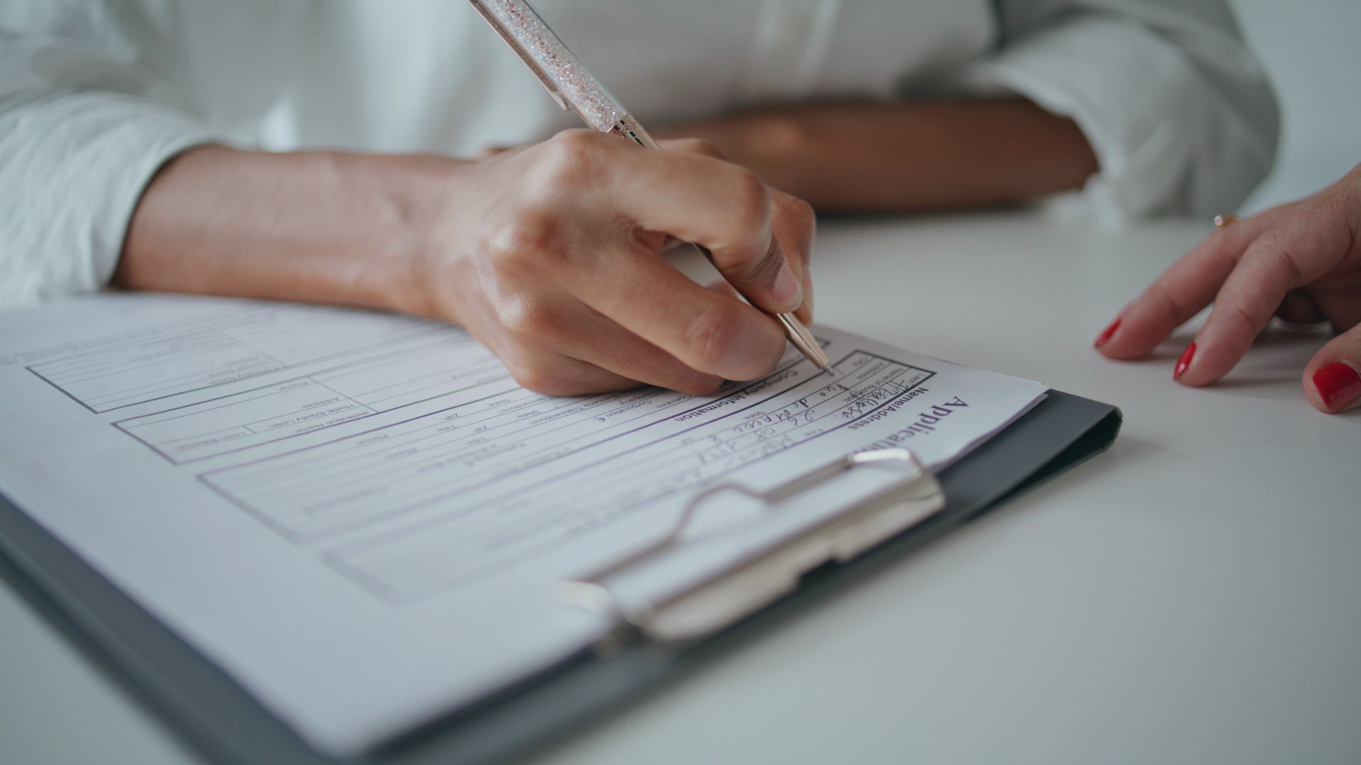 A person is writing on a clipboard with a pen.