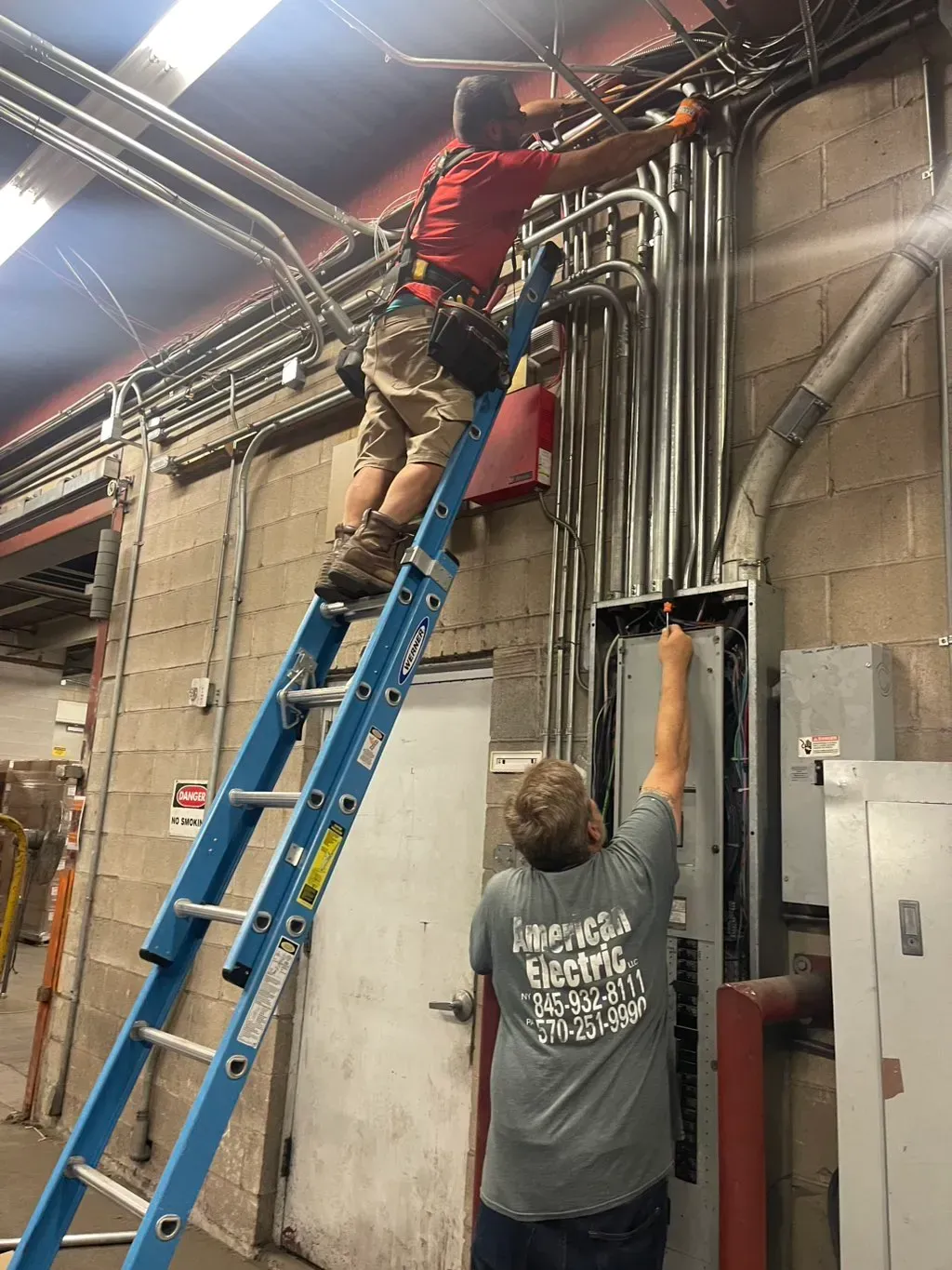 American Electric LLC | A man is standing on a ladder working on an electrical box.