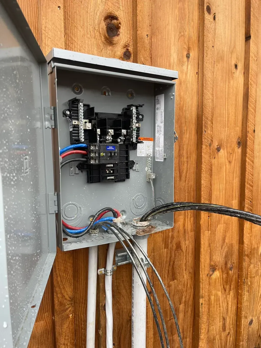 American Electric LLC | A box with wires coming out of it is attached to a wooden fence.