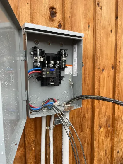 American Electric LLC | A box with wires coming out of it is attached to a wooden fence.
