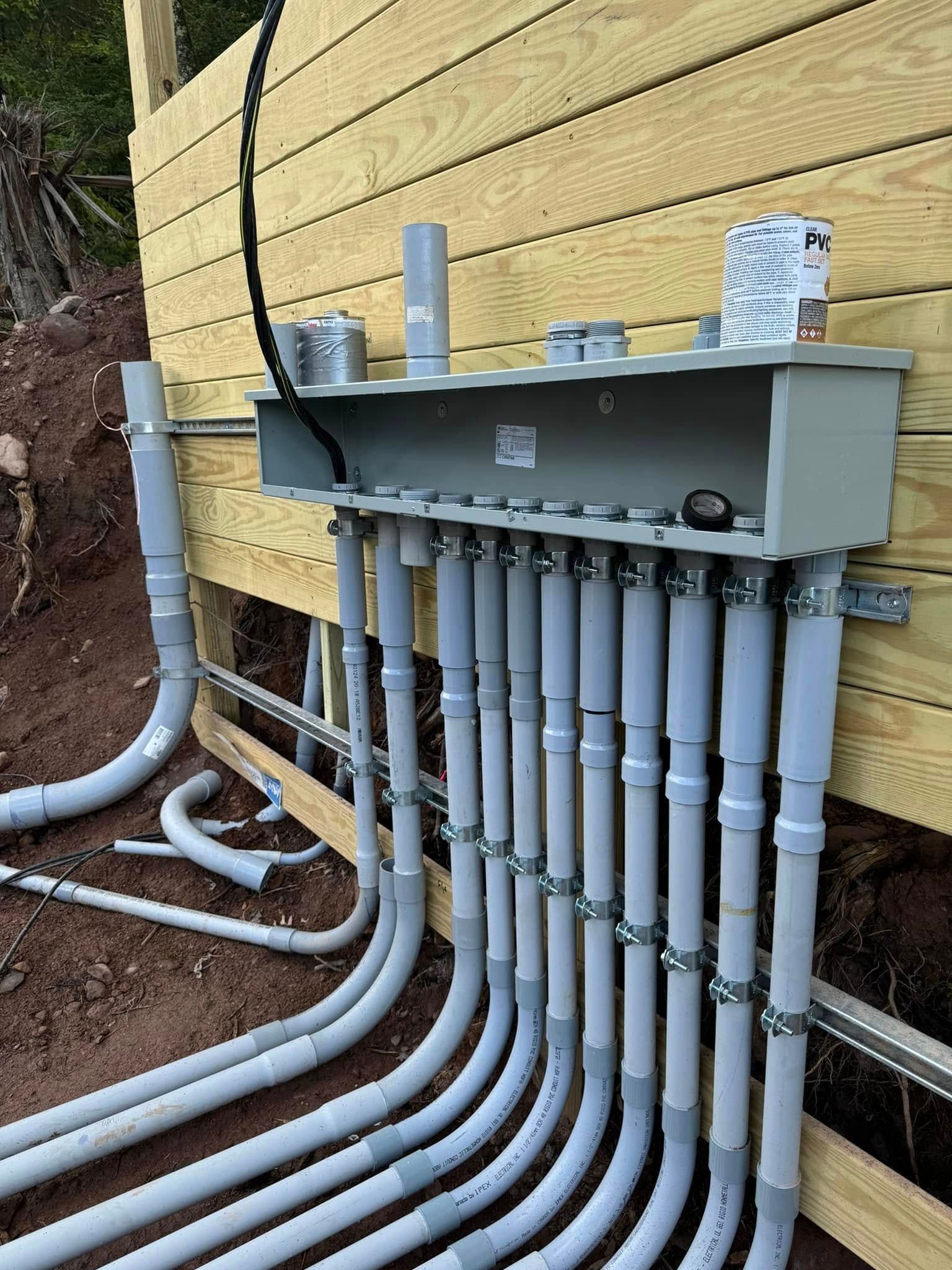 American Electric LLC | A bunch of electrical pipes are connected to a wooden wall.