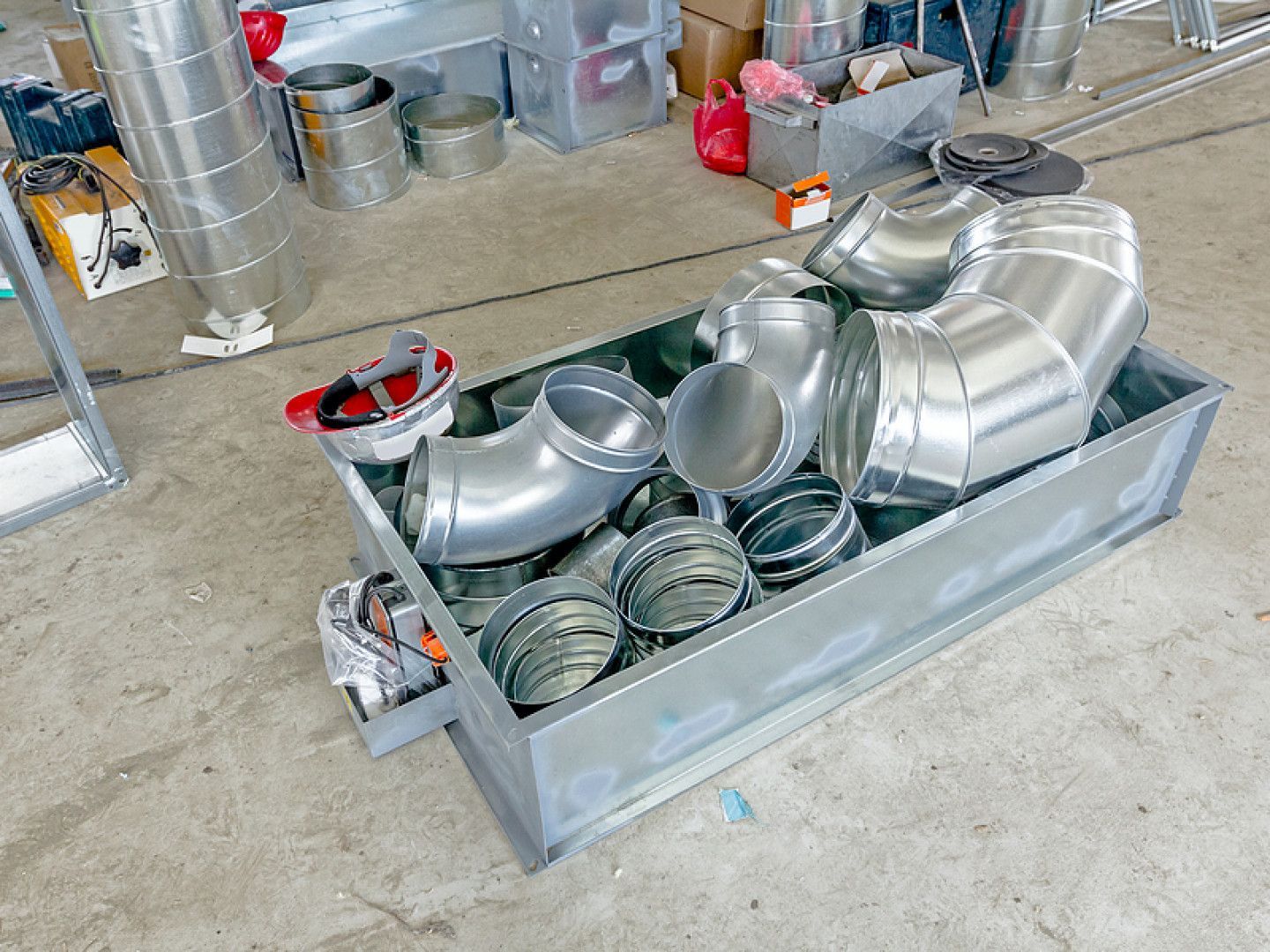 Metal ducting and HVAC fittings arranged in a shallow metal tray in a workshop.