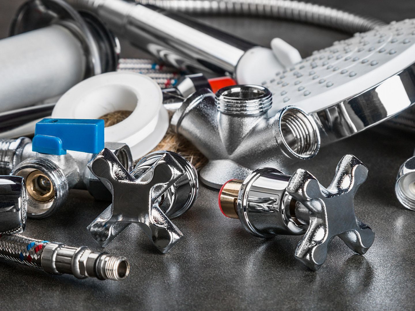 Assorted plumbing fixtures and hoses with chrome valves and connectors on a dark surface