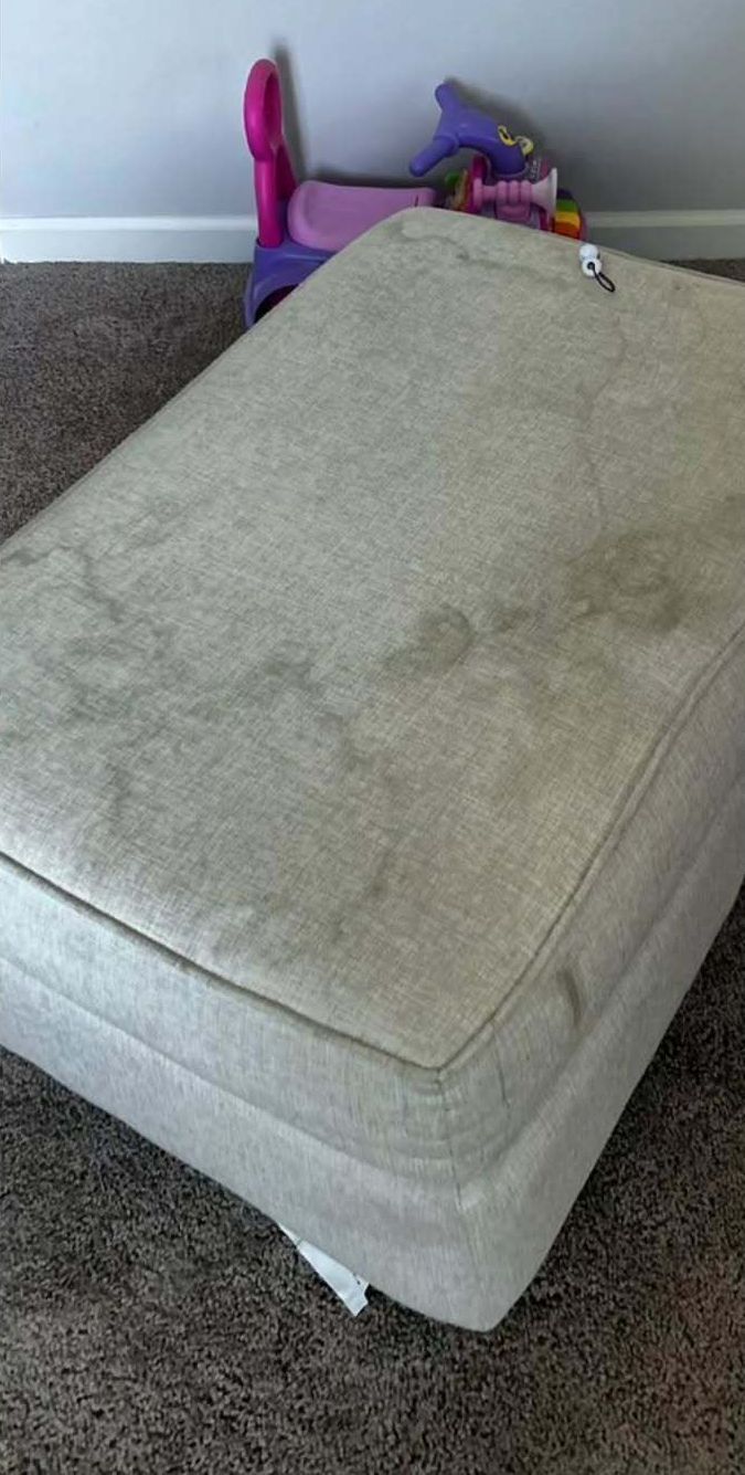 A dirty mattress is sitting on top of a carpeted floor in a room.