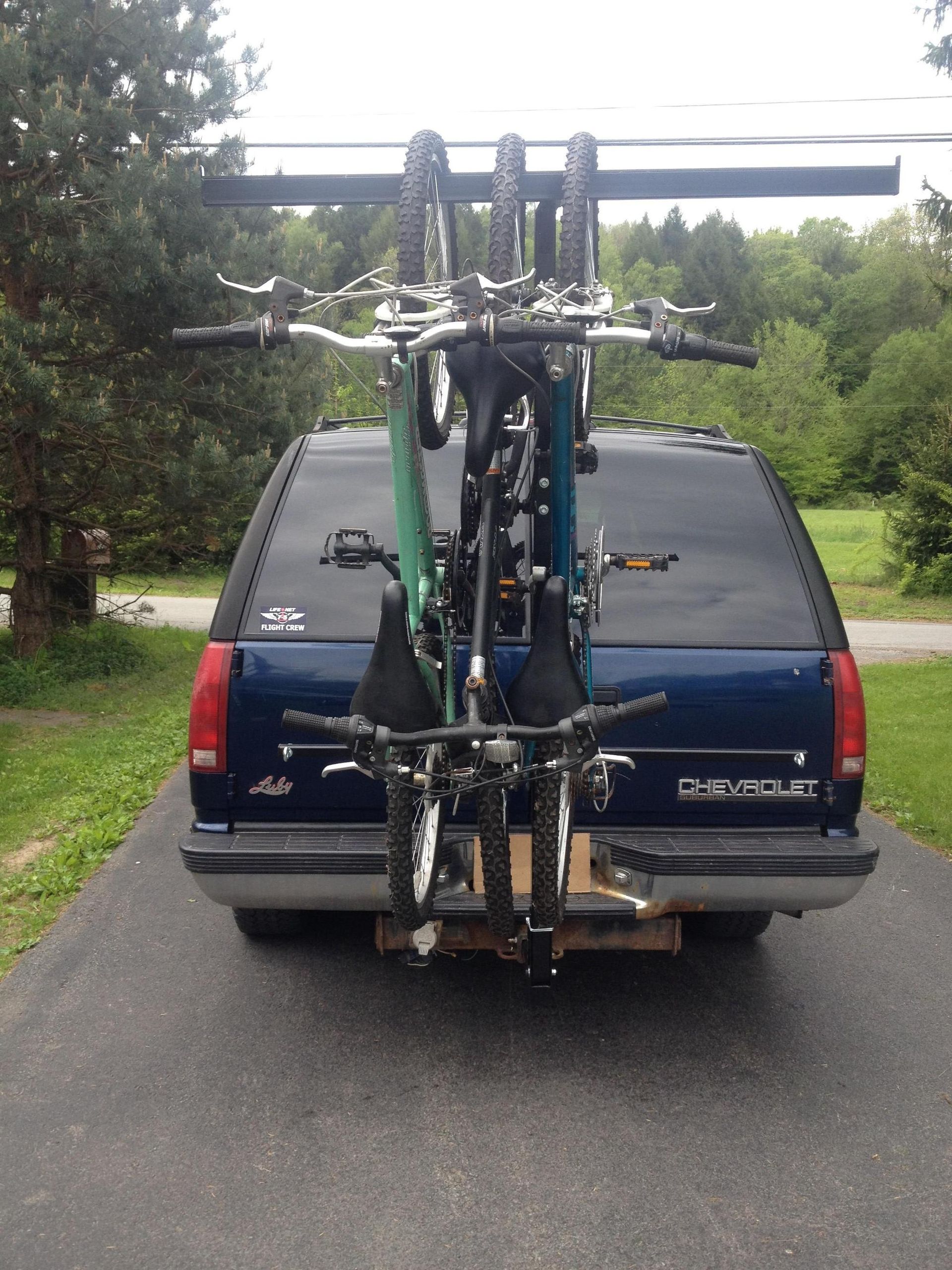 Several bicycles stacked vertically on a rear bike rack on a vehicle in a wooded parking area