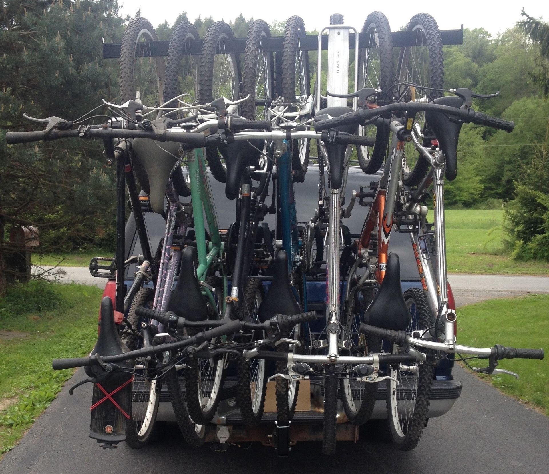 Several bicycles stacked vertically on a rear bike rack on a vehicle in a wooded parking area