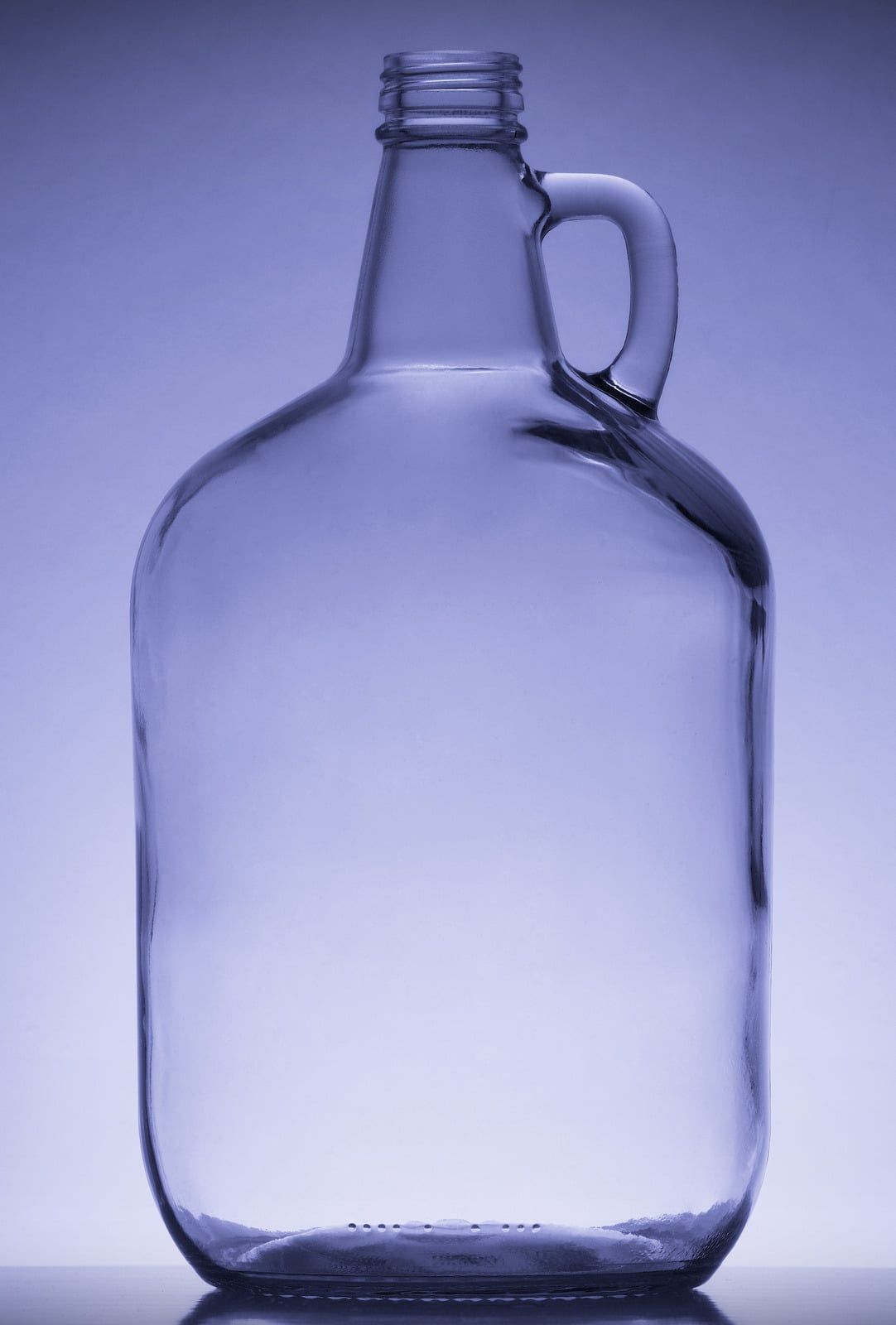 Four empty glass bottles of different heights on a wooden table. A cork and spray bottle are nearby.