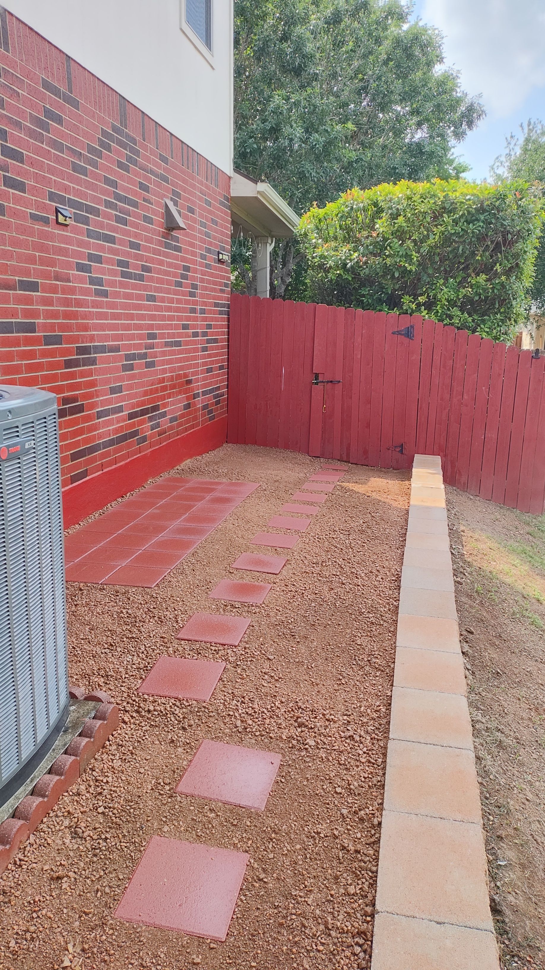 Red brick wall, red fence, stepping stones and gravel pathway beside a building.