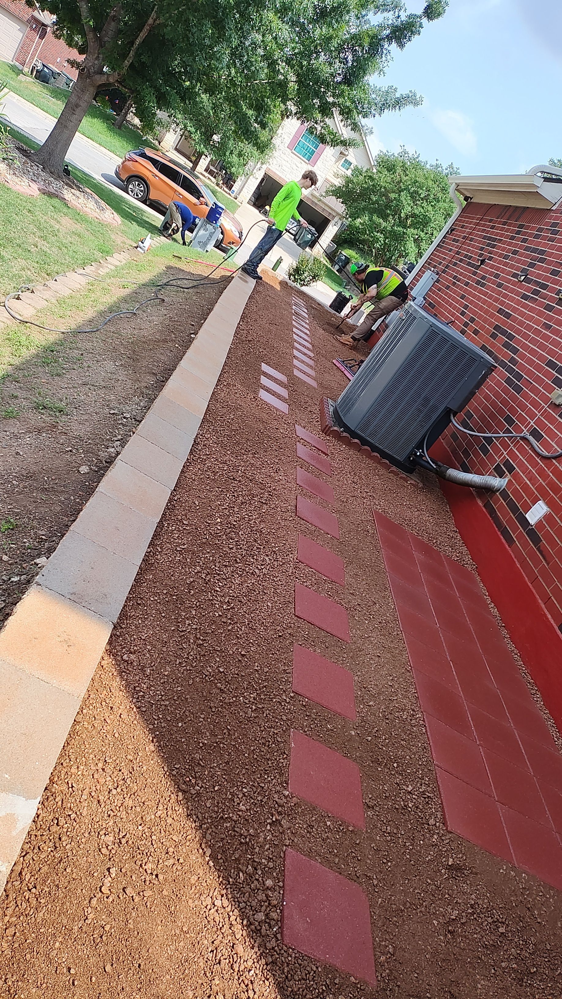 Workers on a roof installing gravel, with a pathway, brickwork, and an air conditioning unit.