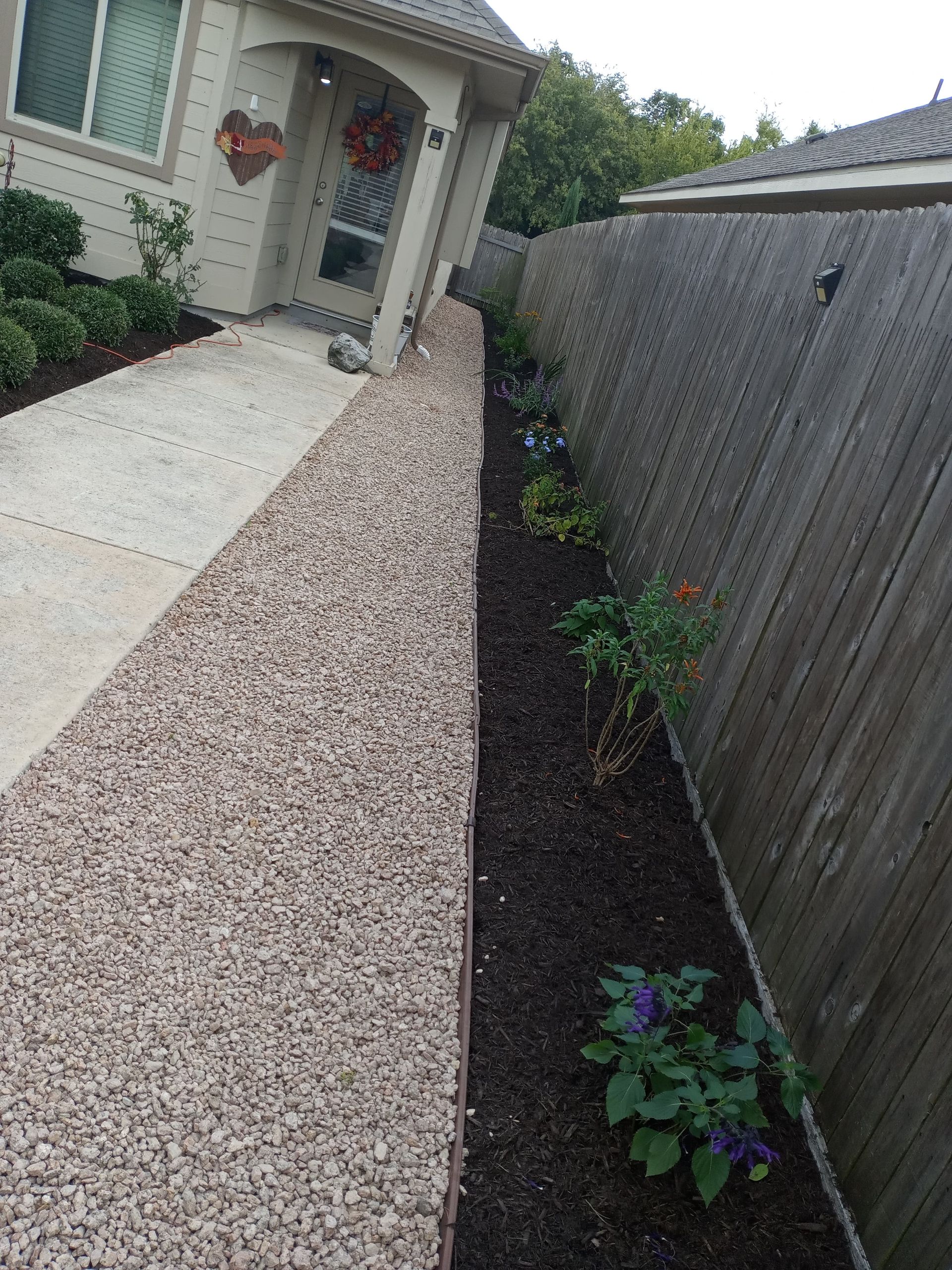 A pathway next to a gravel-covered retaining wall with a landscaped border and wooden fence.